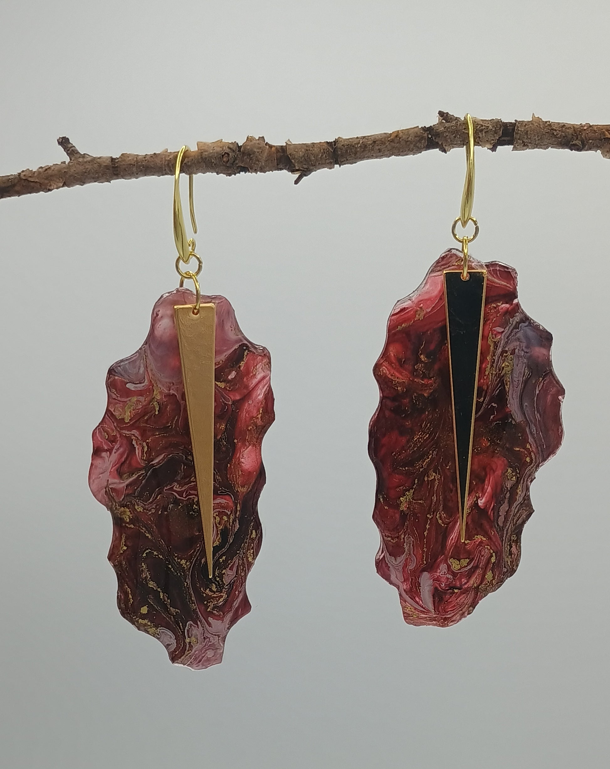Marbled red and gold handmade earrings on a branch against a gray background a Style By Jess