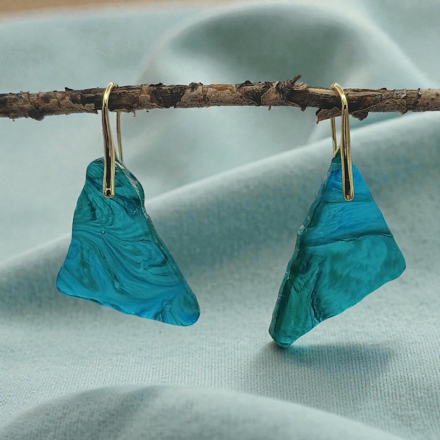 Handmade resin turquoise marbled earrings hanging from a branch on a light blue fabric background gift display a Style By Jess at Gotta Have It Design