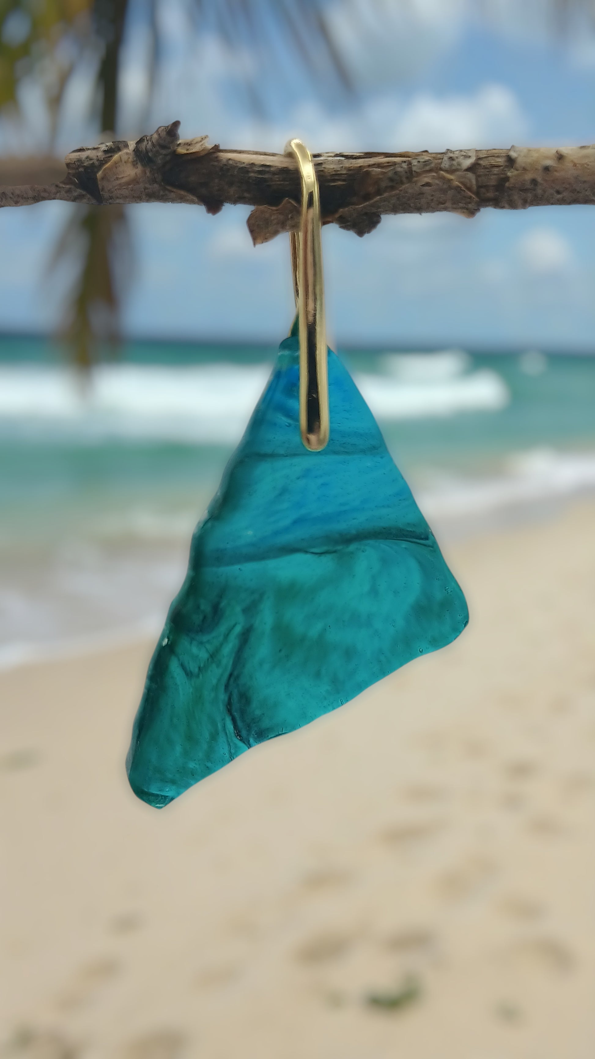 Teal earrings hanging from a branch on a beach with ocean in the background