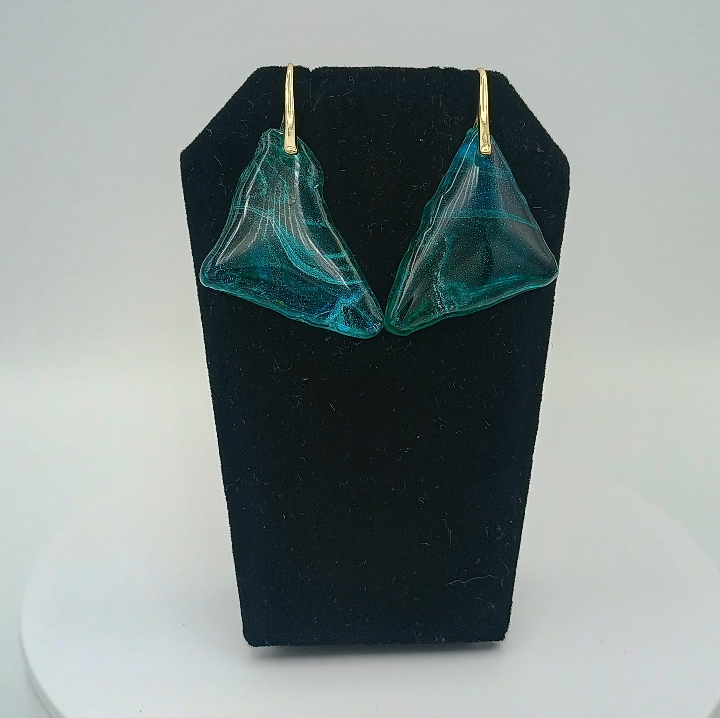 Teal earrings on a black stand against a white background