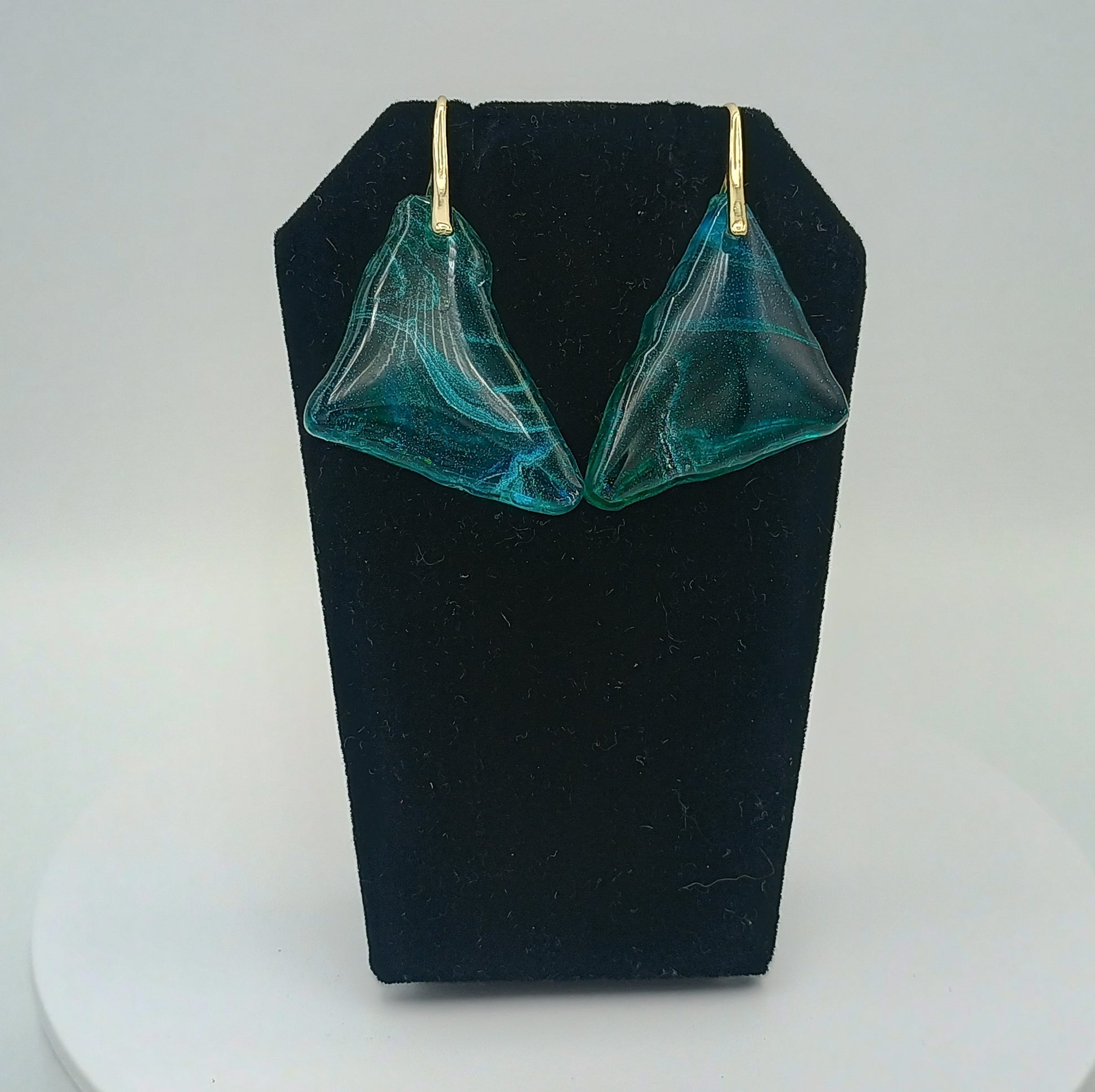 Teal earrings on a black stand against a white background
