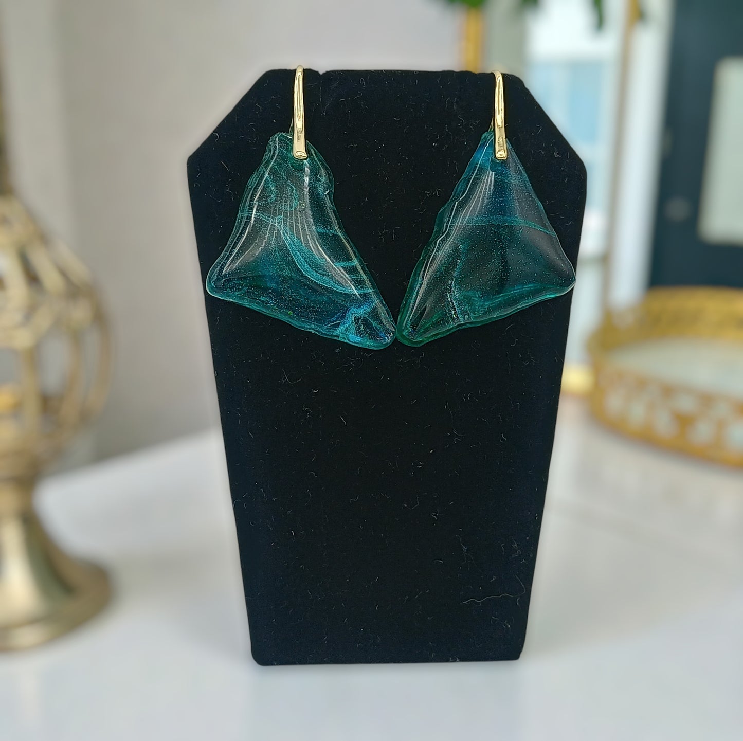 Teal earrings on a black stand with a blurred background
