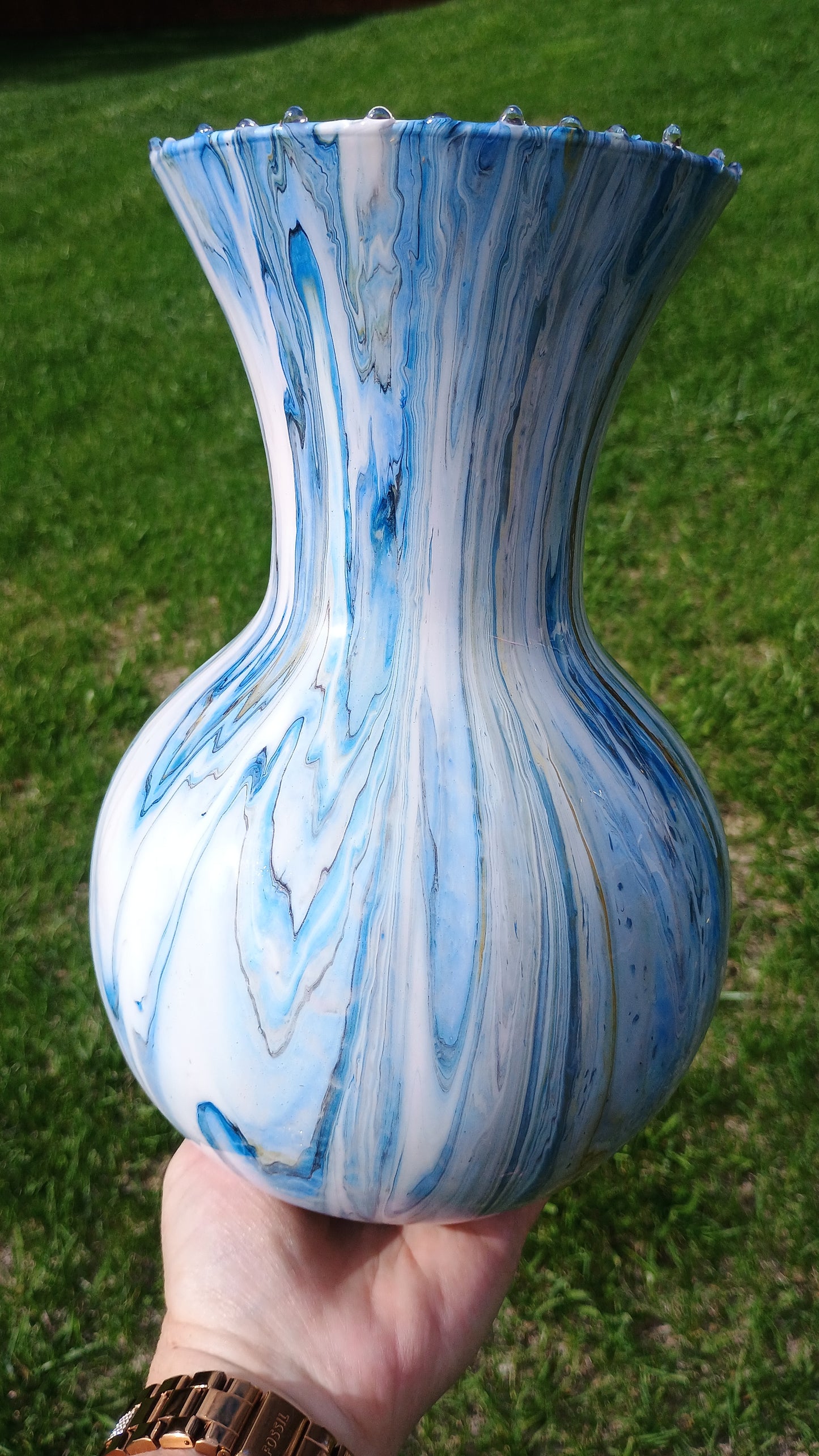 Hand holding a blue and white marbled hand painted vase against a grassy background