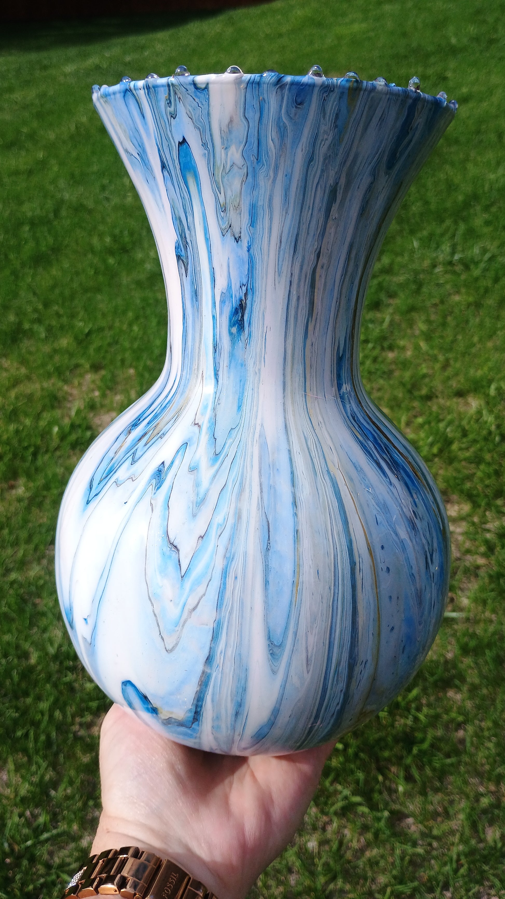 Hand holding a blue and white marbled hand painted vase against a grassy background