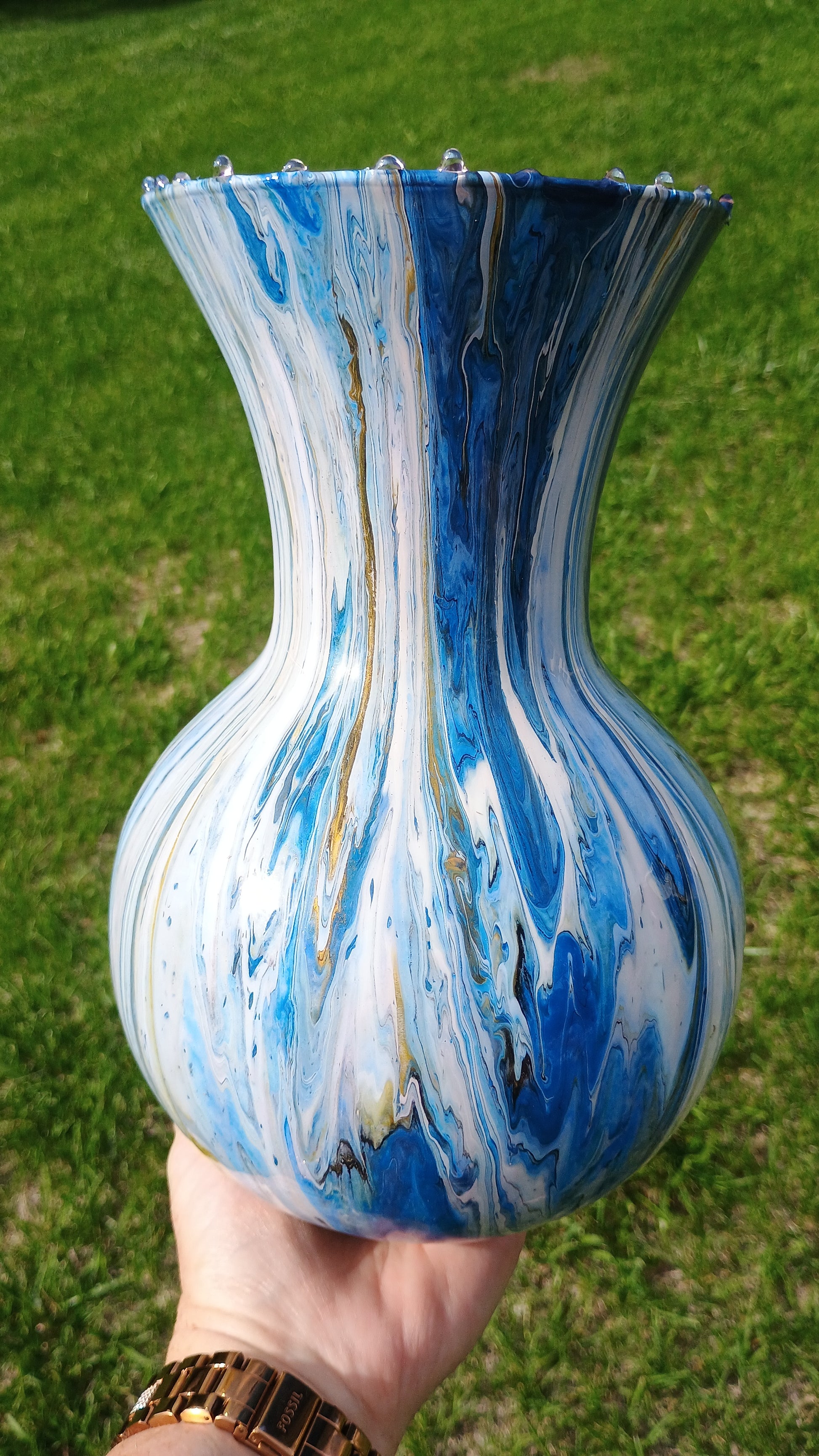 Hand holding a blue and white marbled vase against a green grass background