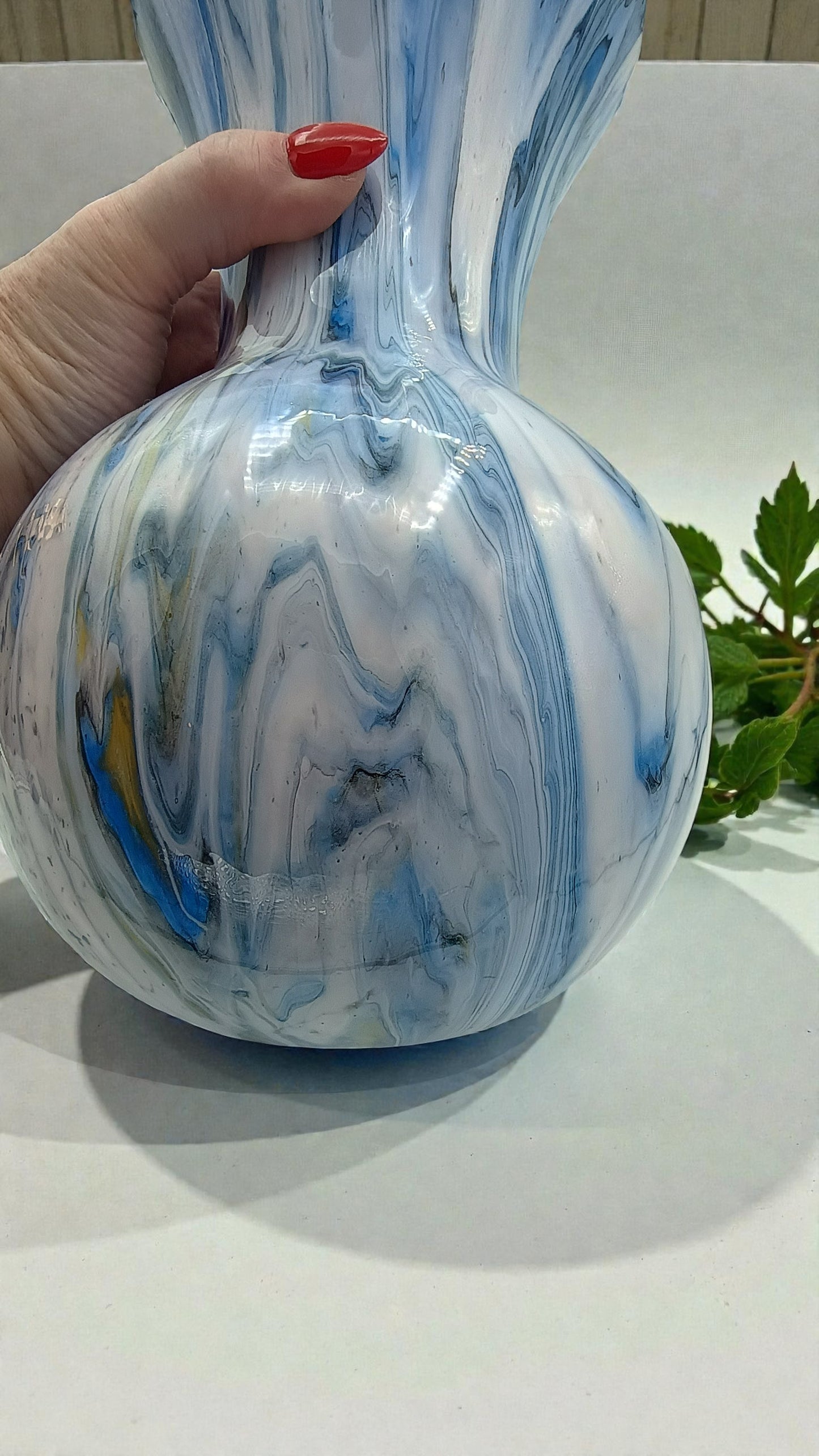Marbled blue and white vase held by a hand with red nail polish on a light background.