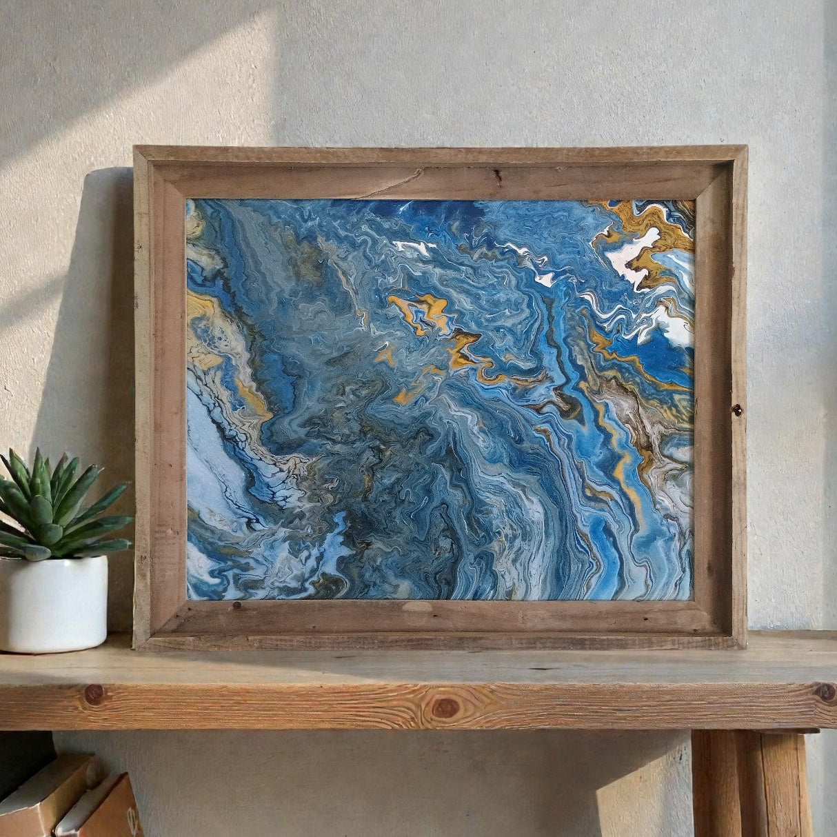 Framed abstract painting with blue and gold tones on a wooden shelf in an office.