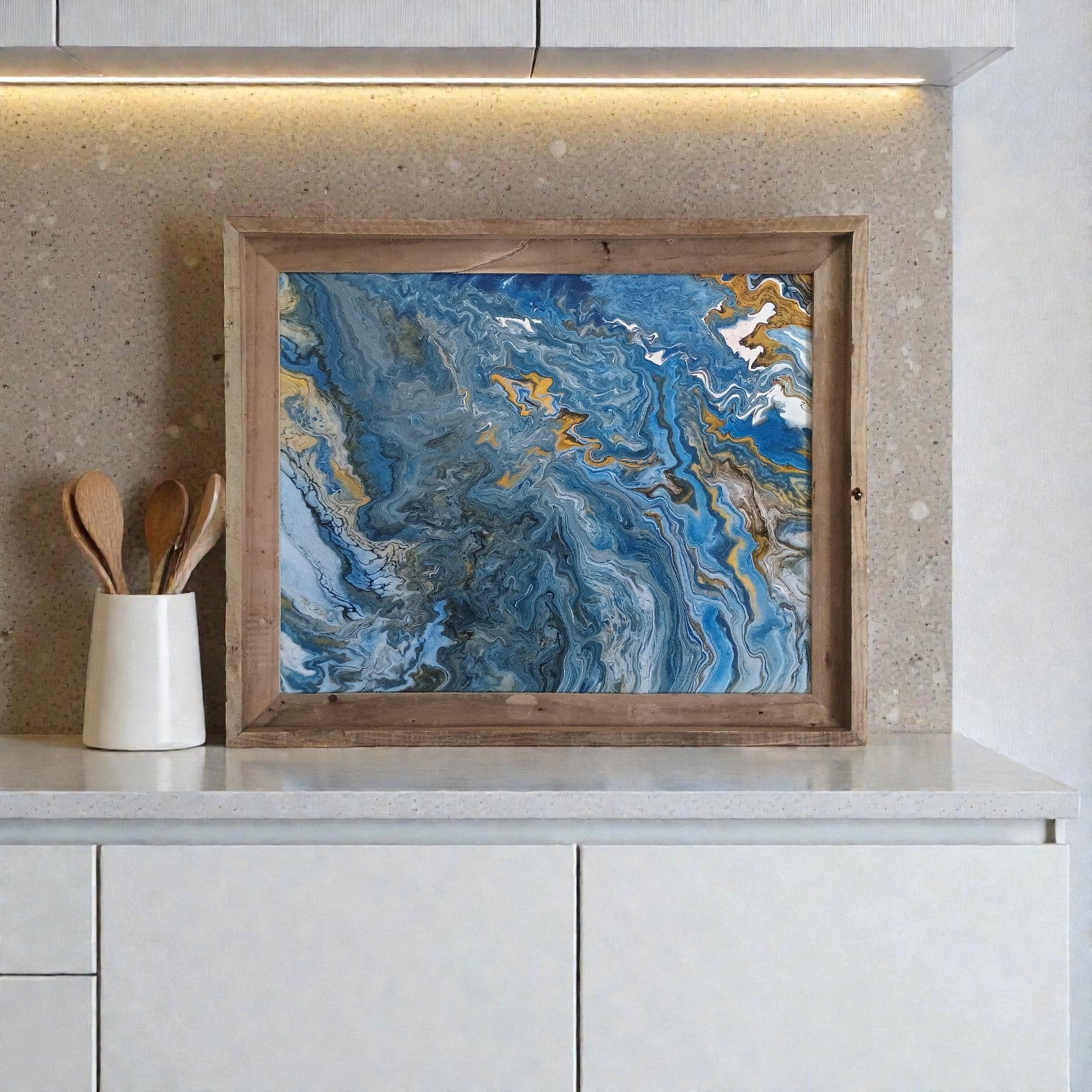 Abstract painting with blue and gold tones in a wooden frame on a kitchen counter.