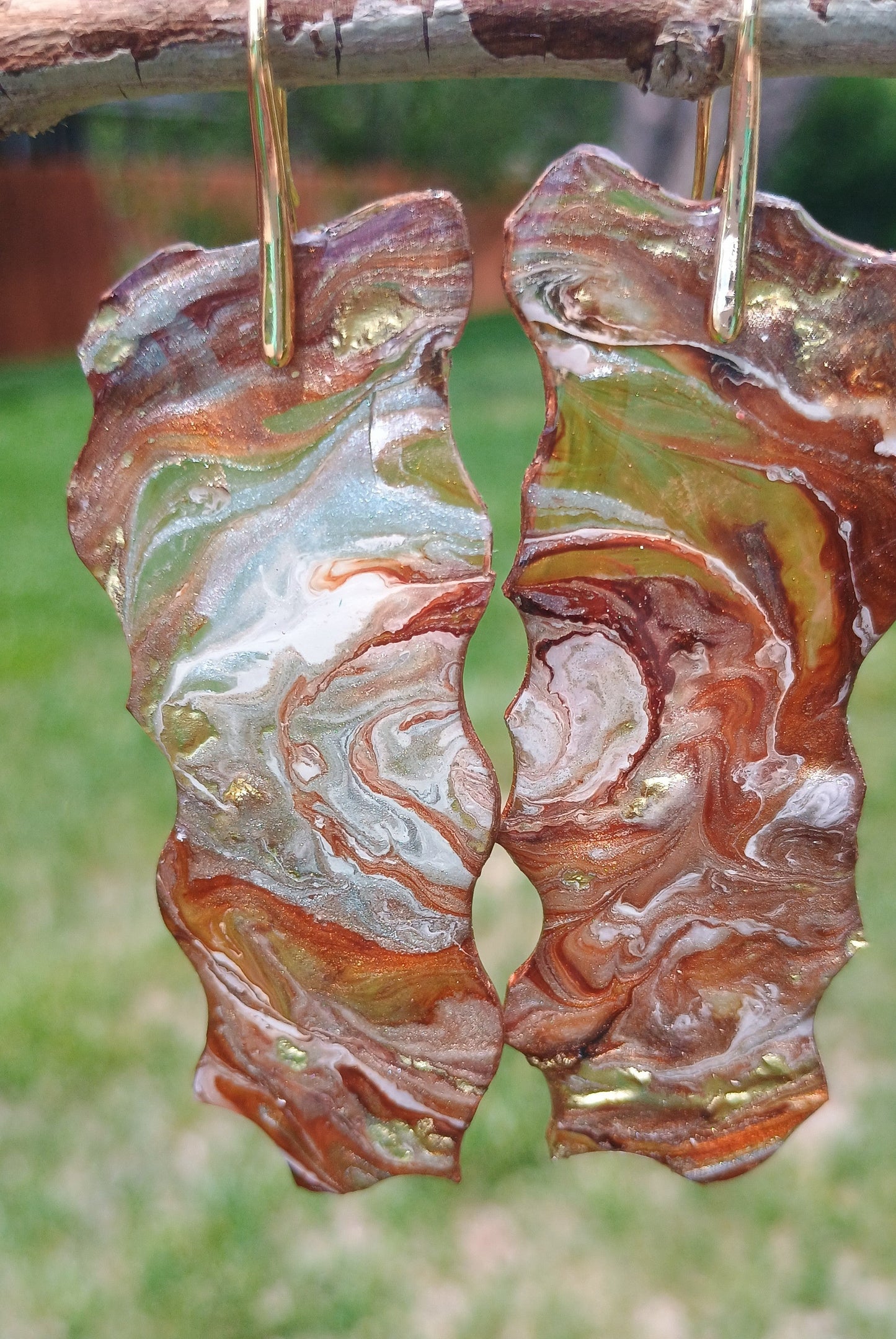 Marbled patterned earrings on a branch with a blurred green background