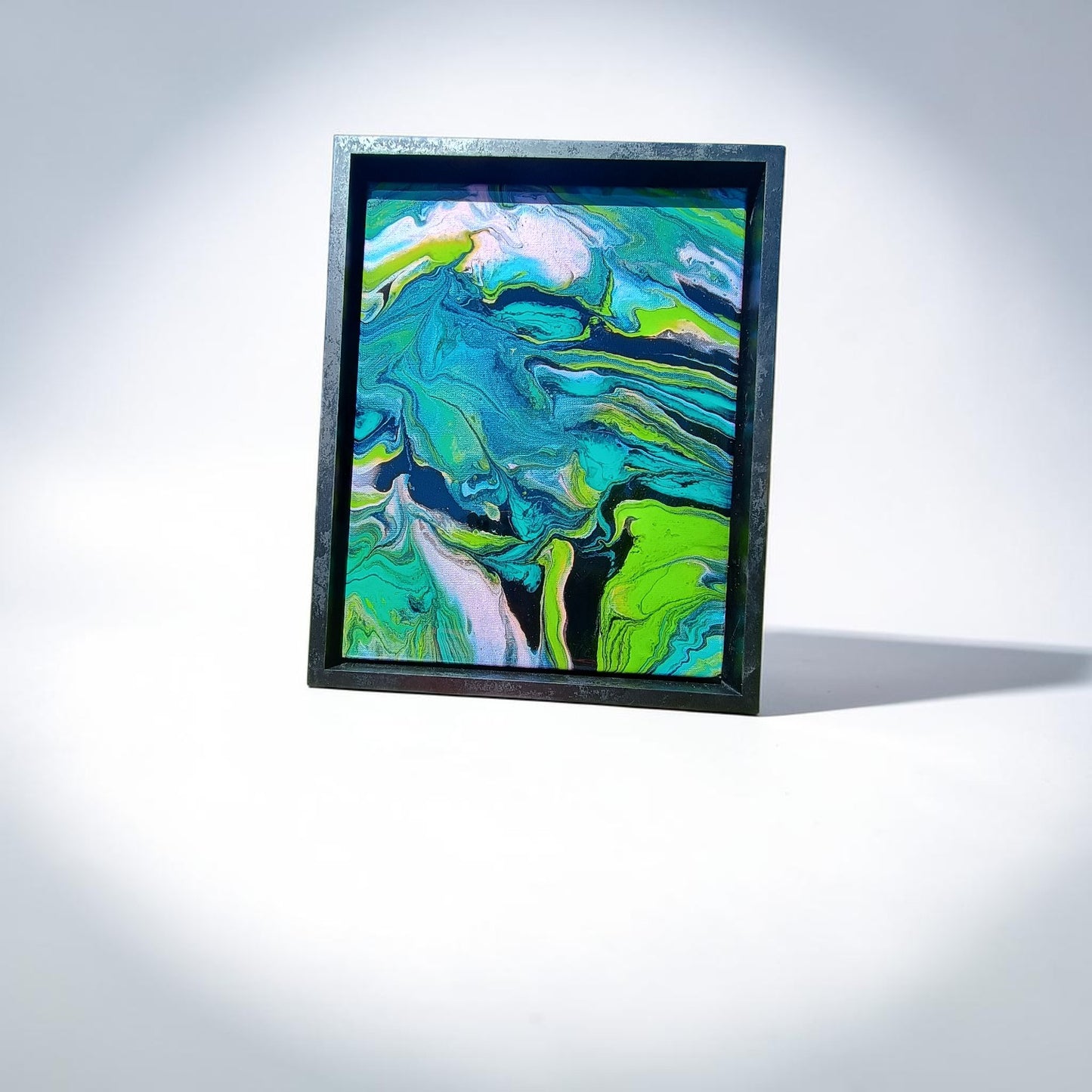 Framed abstract artwork with swirling green, blue, and white colors on a light gray background