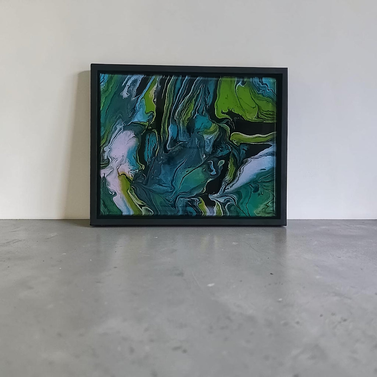 Framed abstract painting with green and blue tones on a white wall.