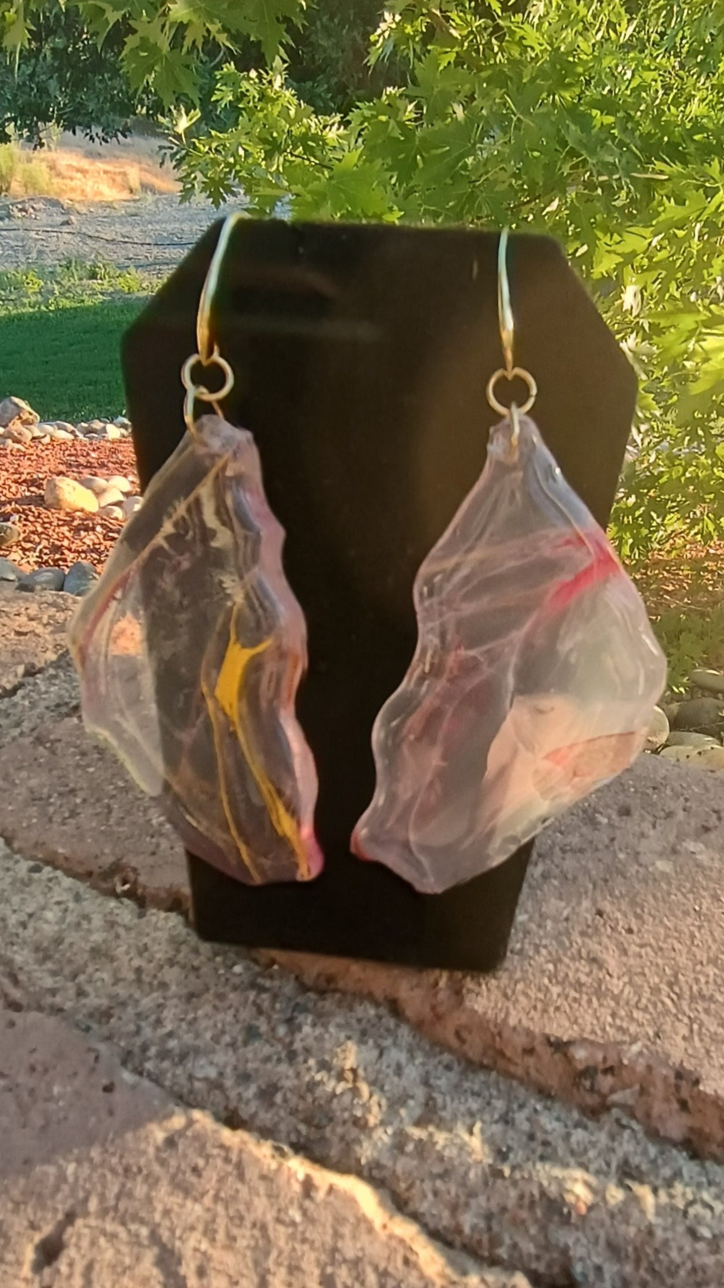 Translucent resin earrings on a black stand with a natural outdoor background