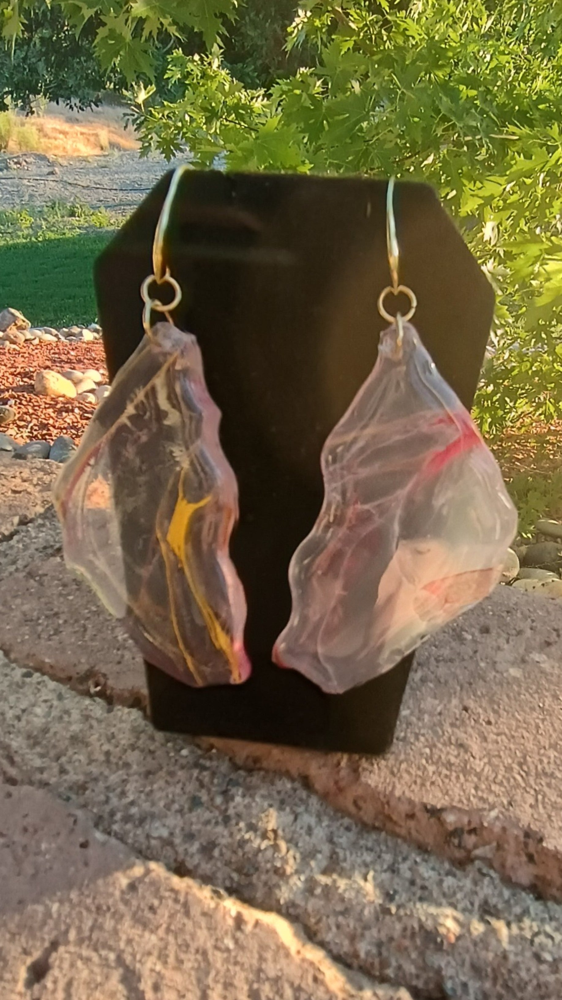 Translucent resin earrings on a black stand with a natural outdoor background