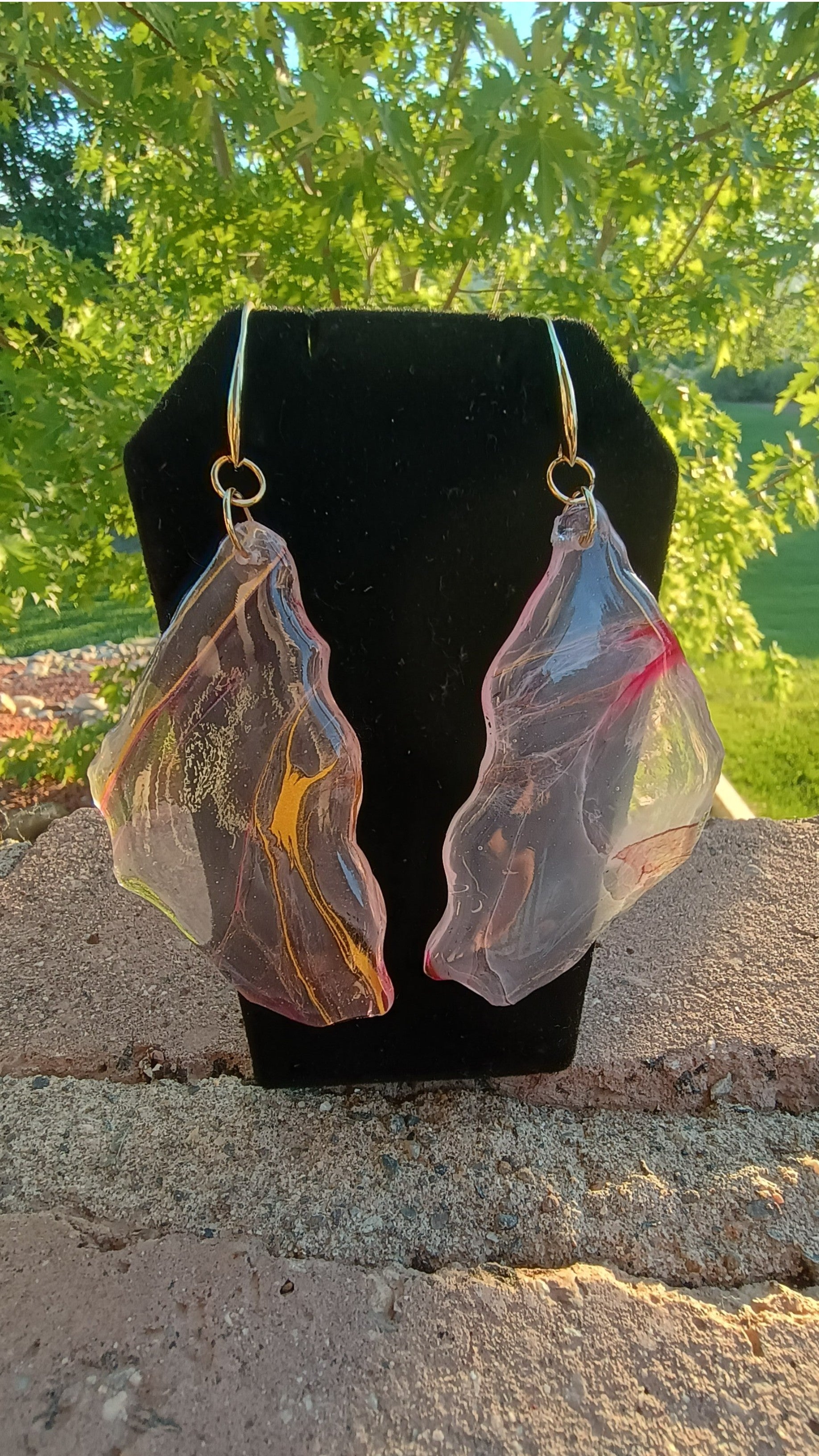 Pair of glass looking earrings on a black stand with a natural background