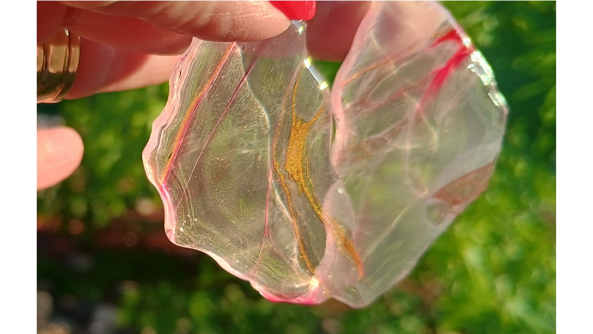 Close up of translucent resin earrings handmade one of a kind with a hand holding them and a nature background blurred. 