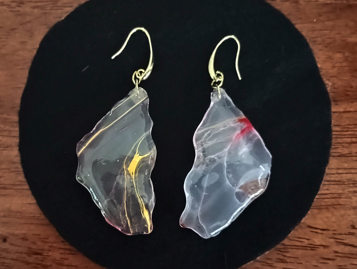 Translucent dangle earrings with gold and red accents on a black circular stand a Style By Jess at Gotta Have It Design