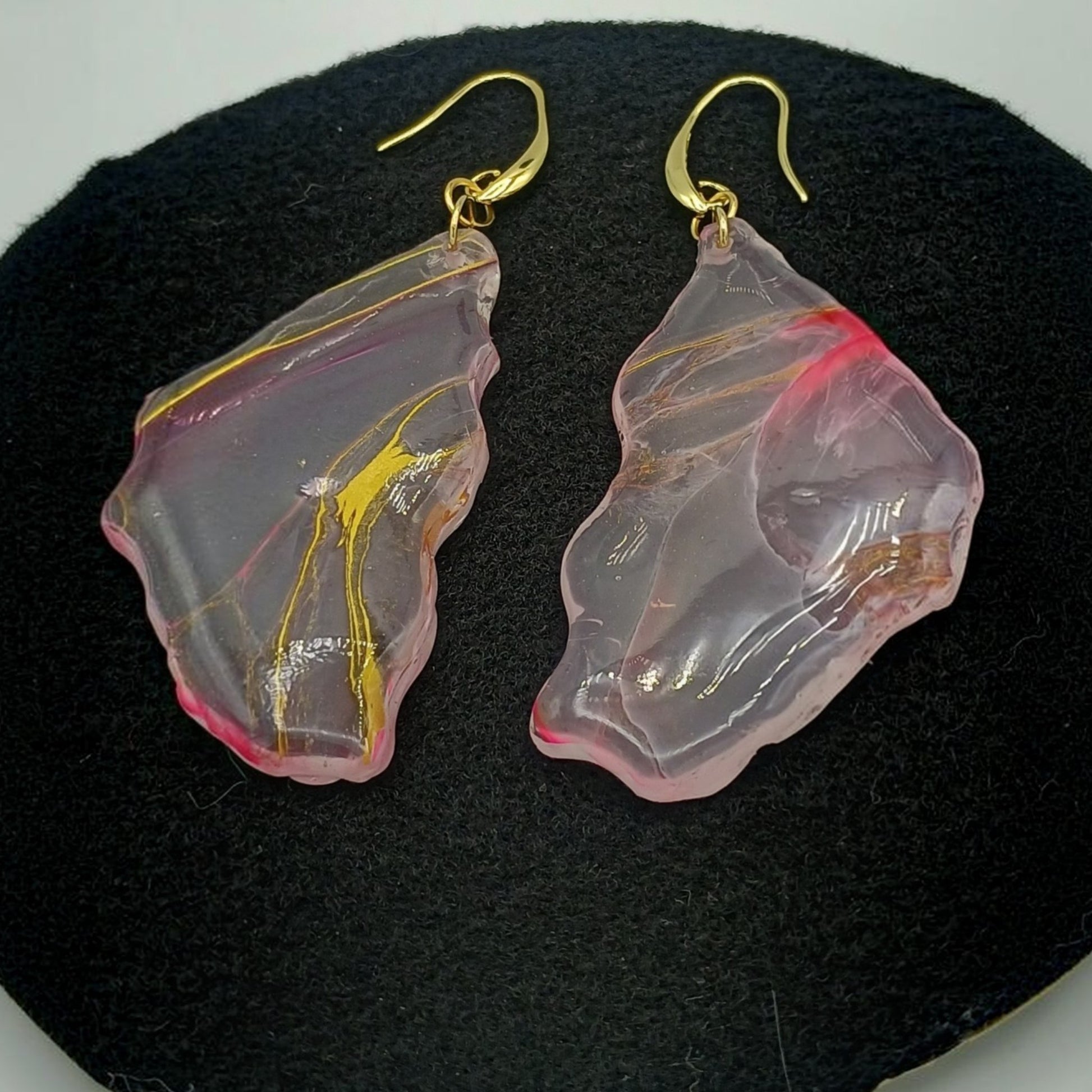 Pink and gold leaf-shaped earrings on a black stand