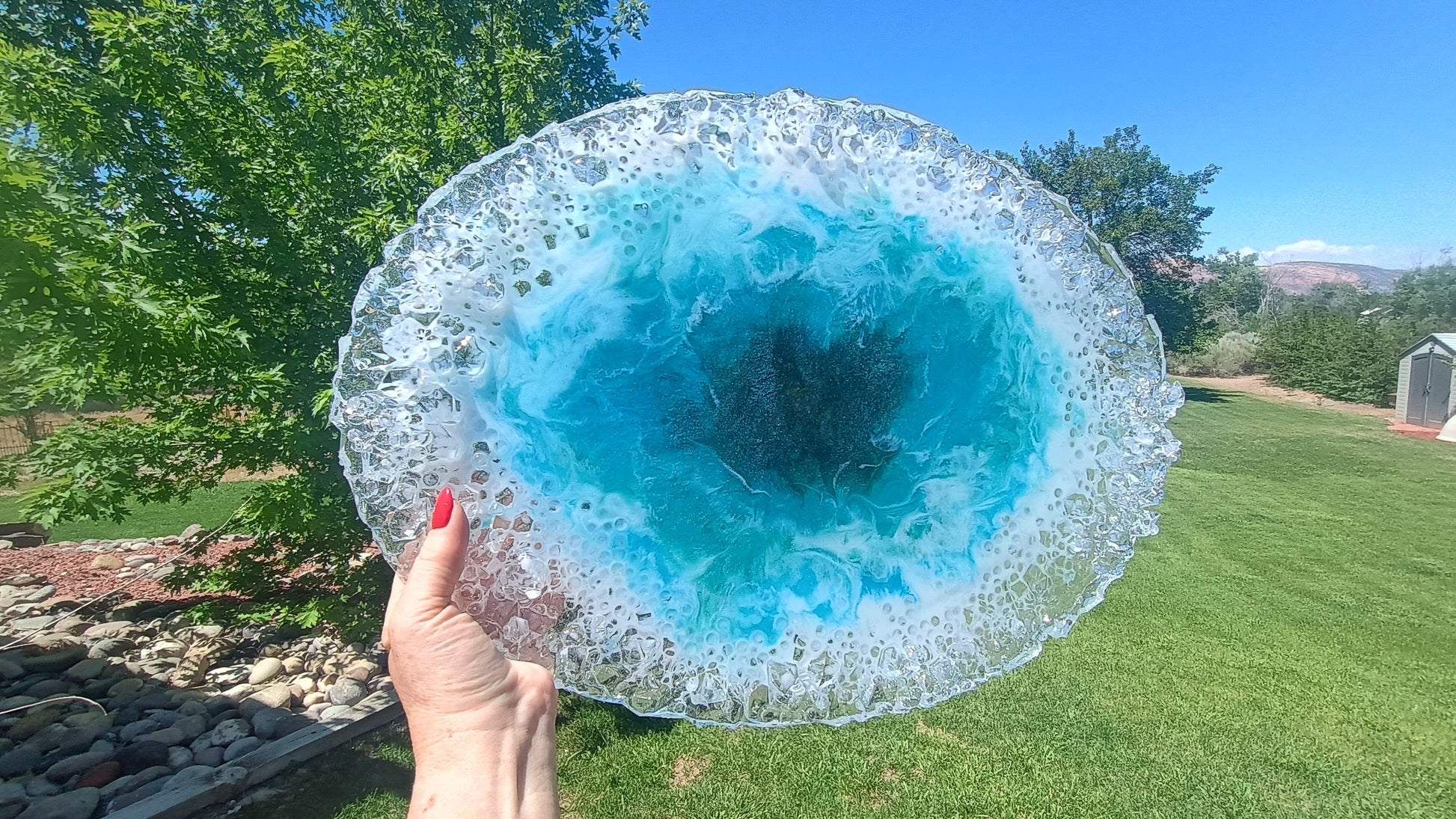 Handmade oversized 20x14 inch food-safe resin art platter held up against a bright blue sky, showcasing a stunning ocean-inspired abstract design in vivid teal, blue, and white with a high-gloss glass-like finish — one-of-a-kind original by Style By Jess at Gotta Have It Design

