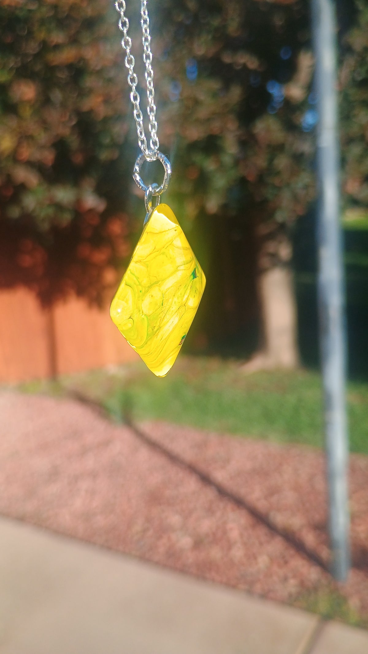 Angled view of double-sided yellow acrylic art pendant suspended from a silver chain