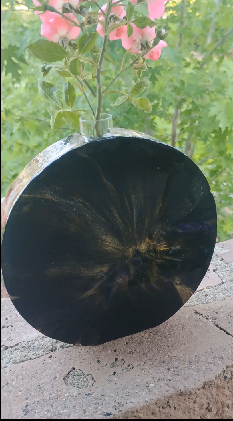 Black and gold resin propaganda vase back side view on a concrete surface with greenery in the background.