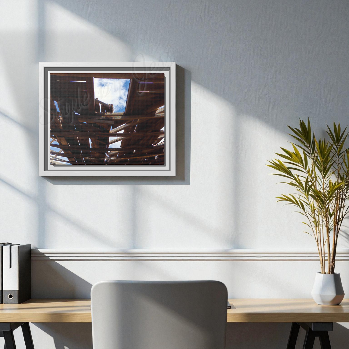 Framed artwork on a wall above a desk with a plant and office supplies.
