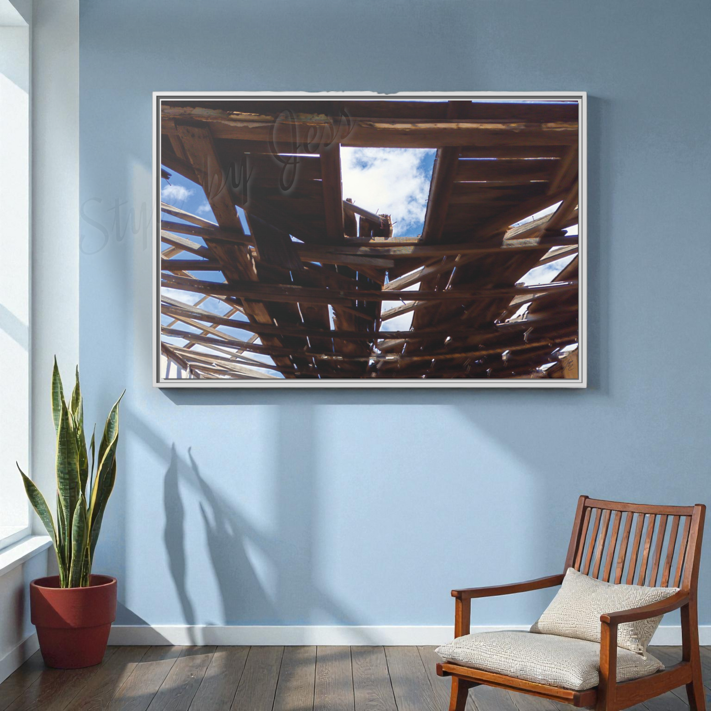 Framed artwork on a blue wall with a wooden chair and plant below.