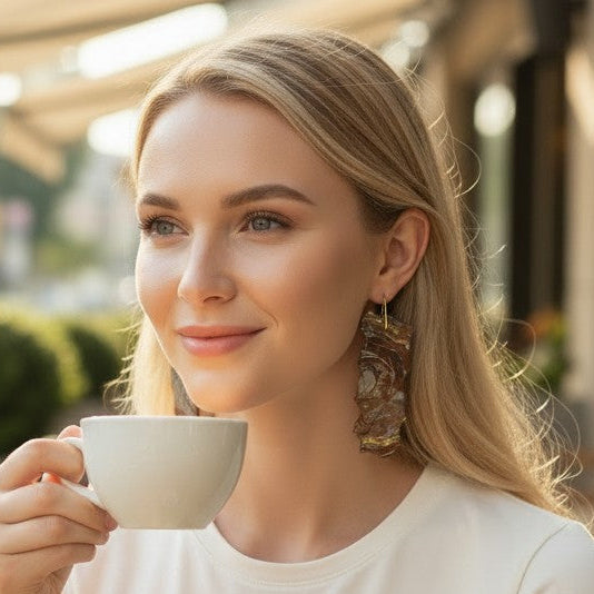 Woman enjoying a cup of coffee outdoors in a casual setting showing off her new dangle earrings.