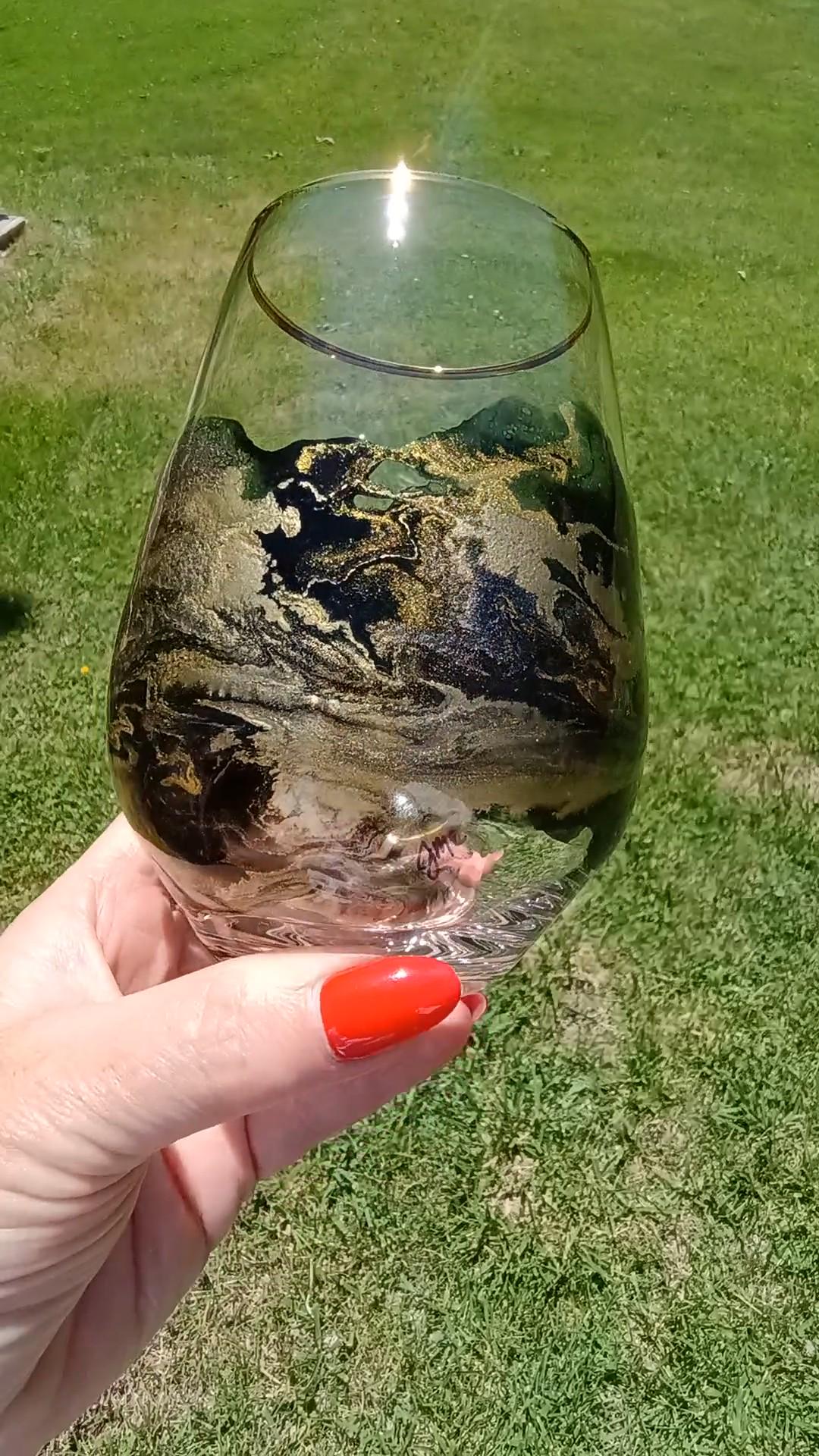 Stemless Win Glass with a black and gold abstract design, held by a person with red nail polish on a grassy background