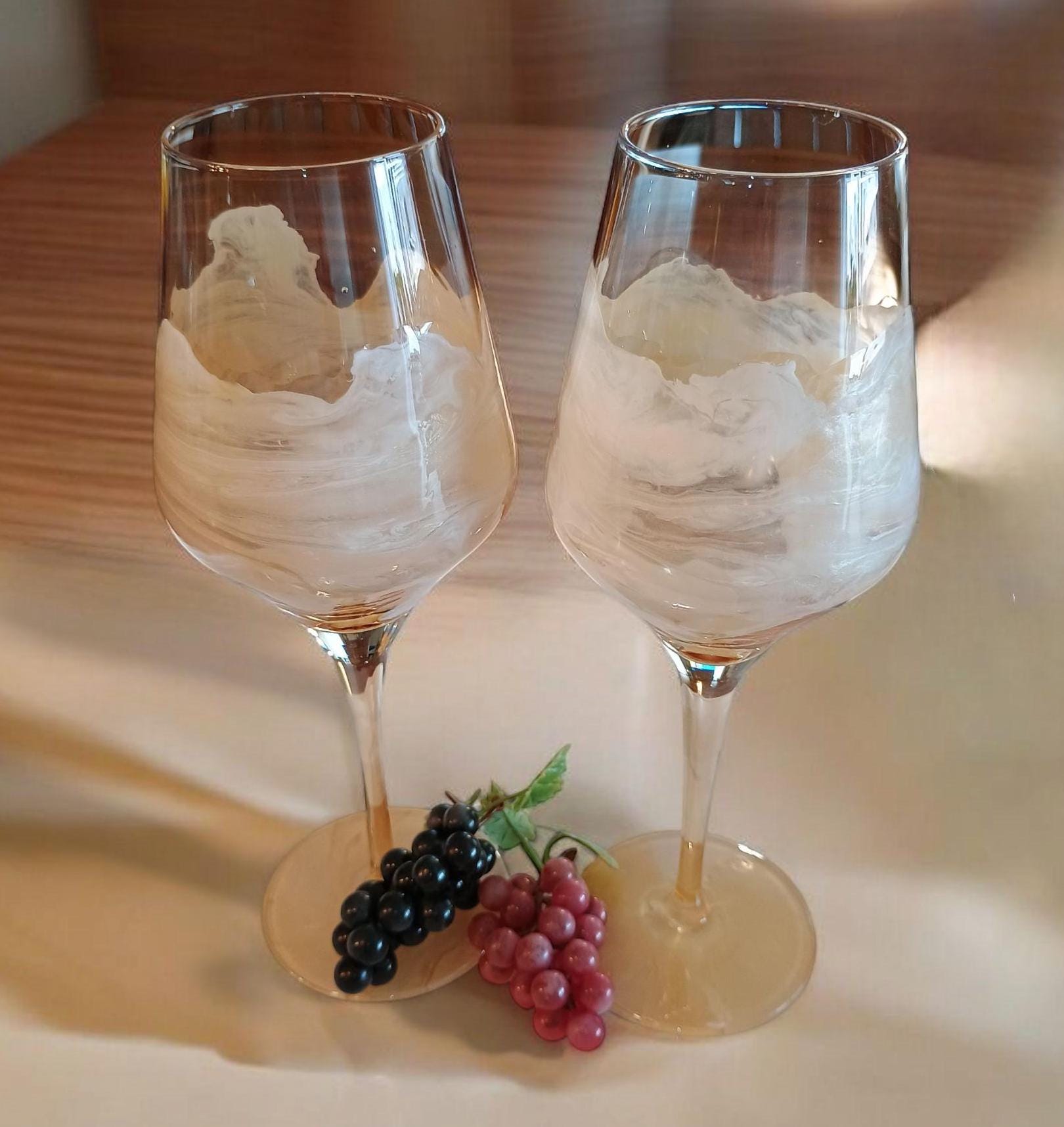 Two wine glasses with a white creamy substance on a wooden surface with grapes.