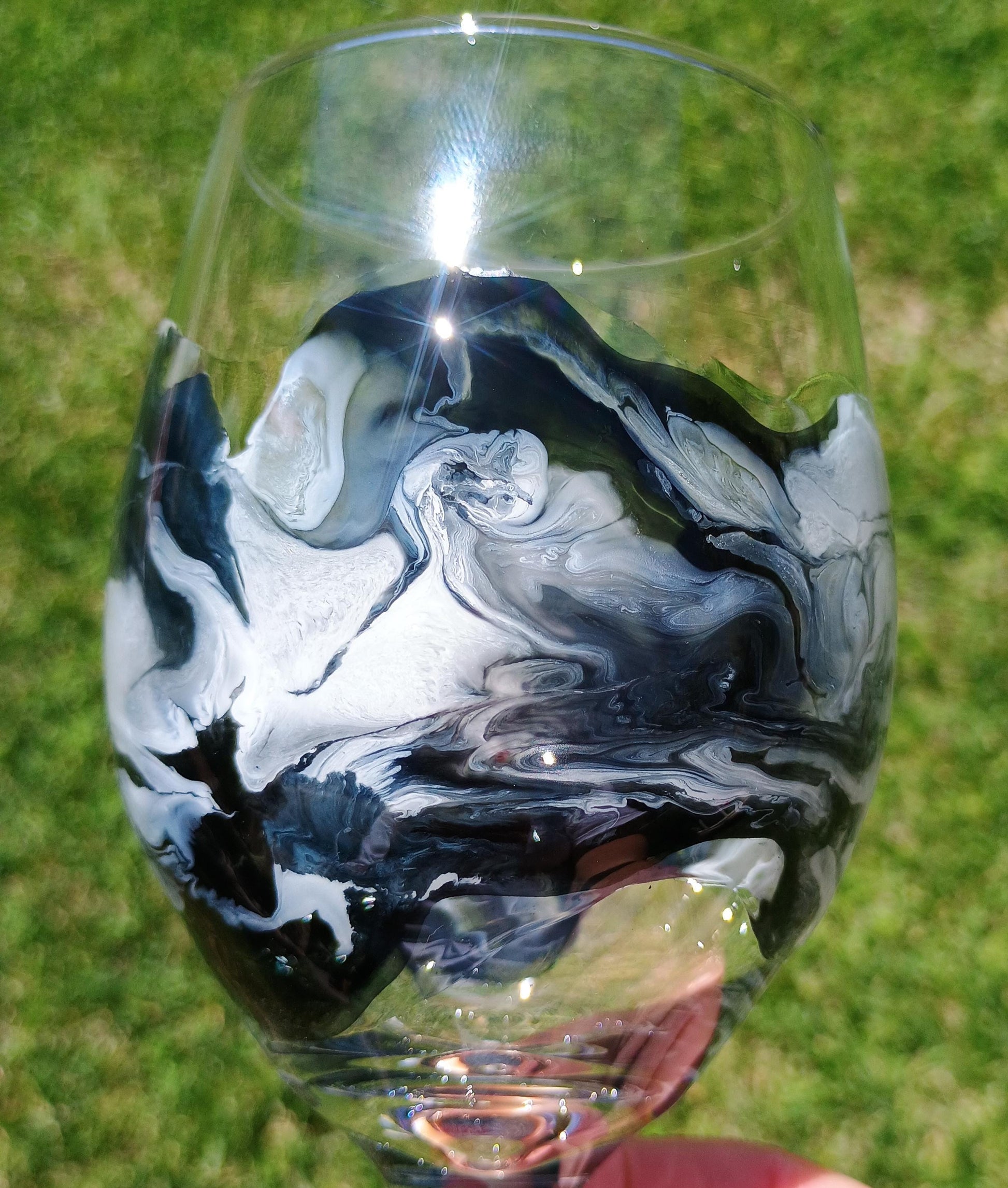Wine glass with black and white marbled design held against a grassy background