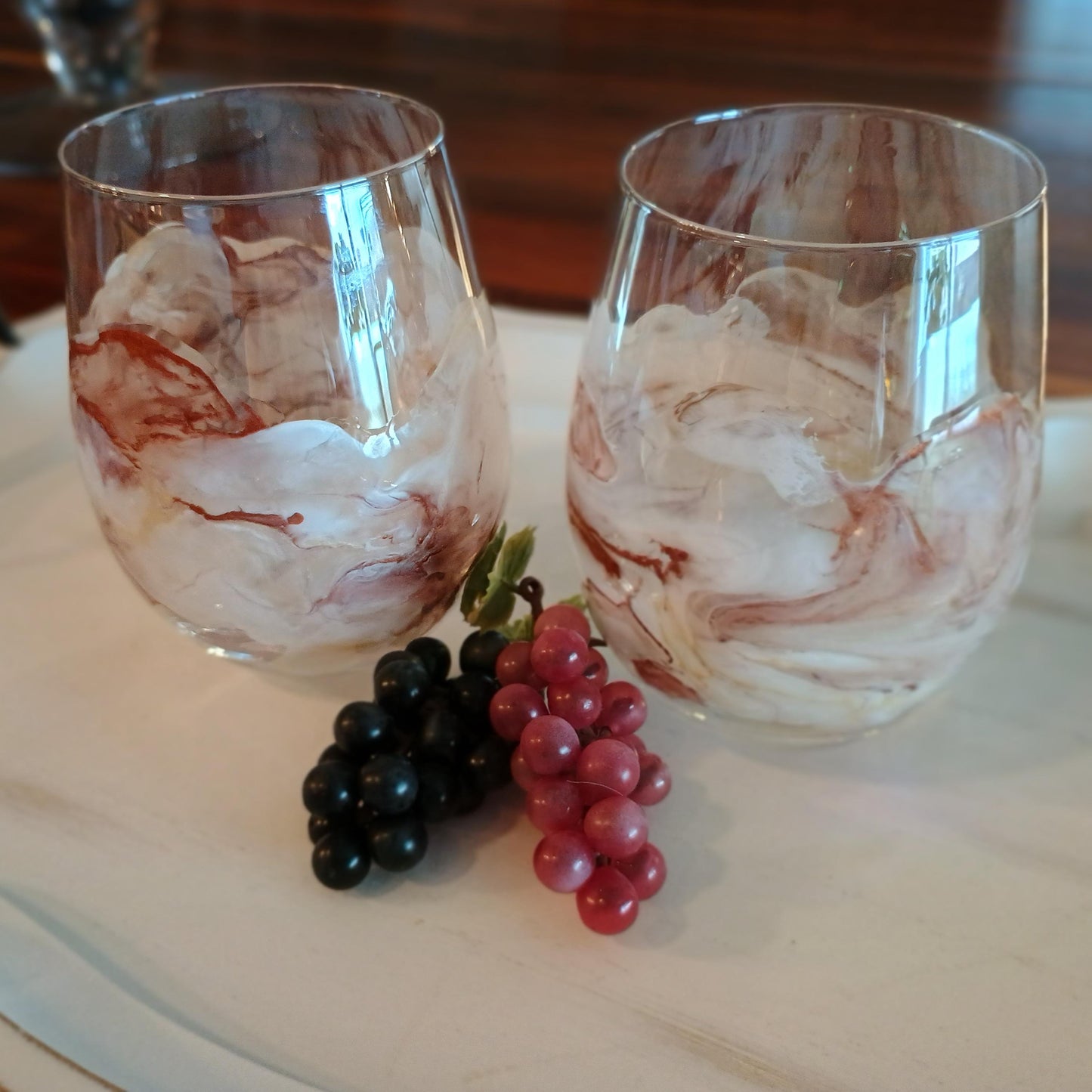 Two marbled wine glasses with grapes on a wooden surface