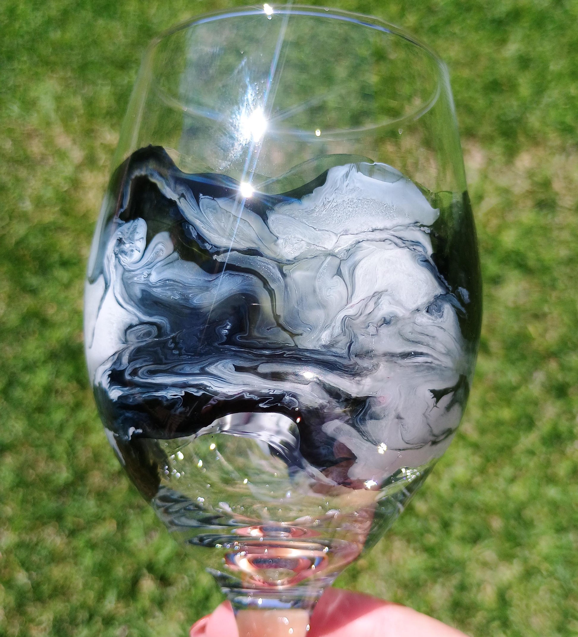 Marbled black and white wine glass held against a grassy background