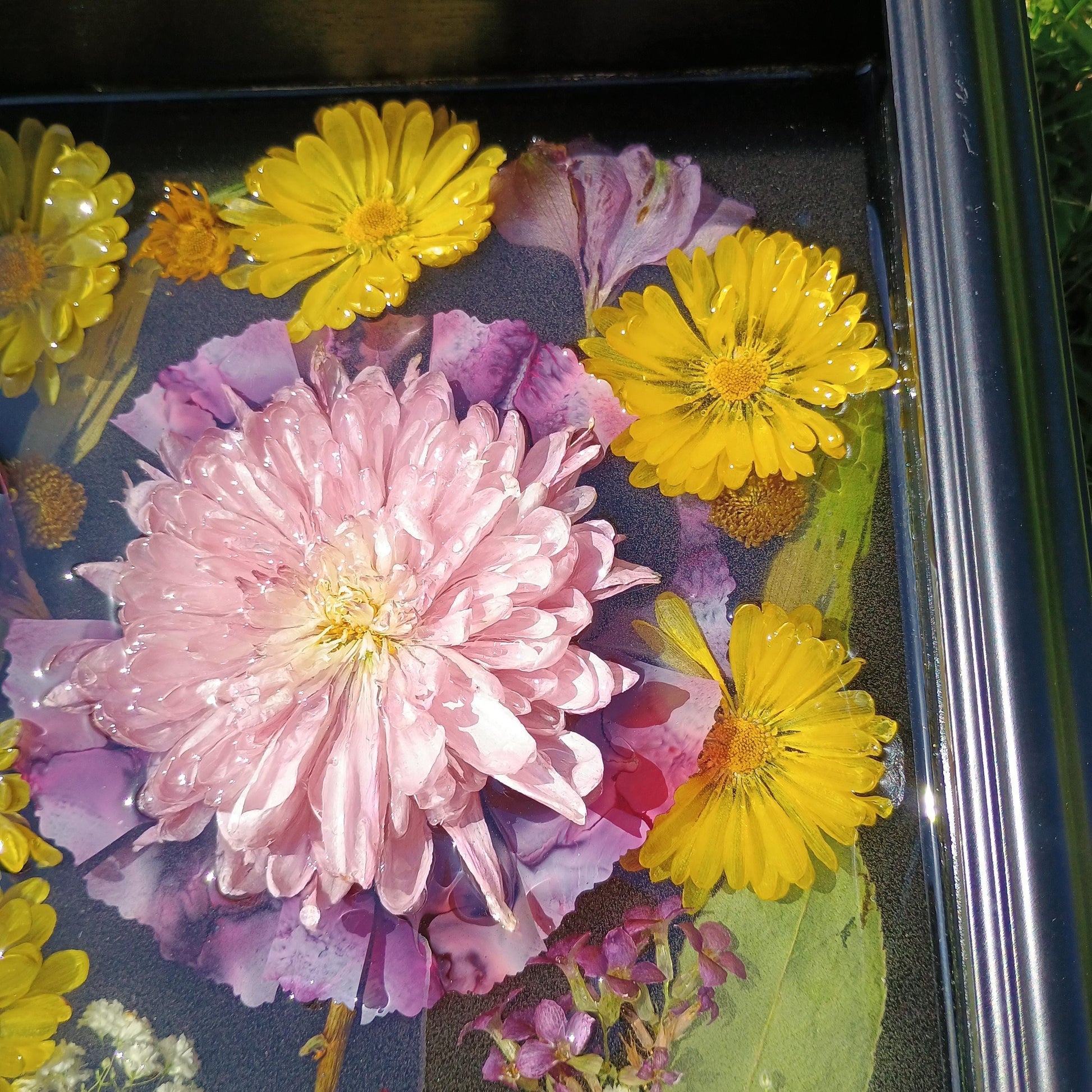 Recessed flowers in resin including pink and yellow blossoms on a dark surface
