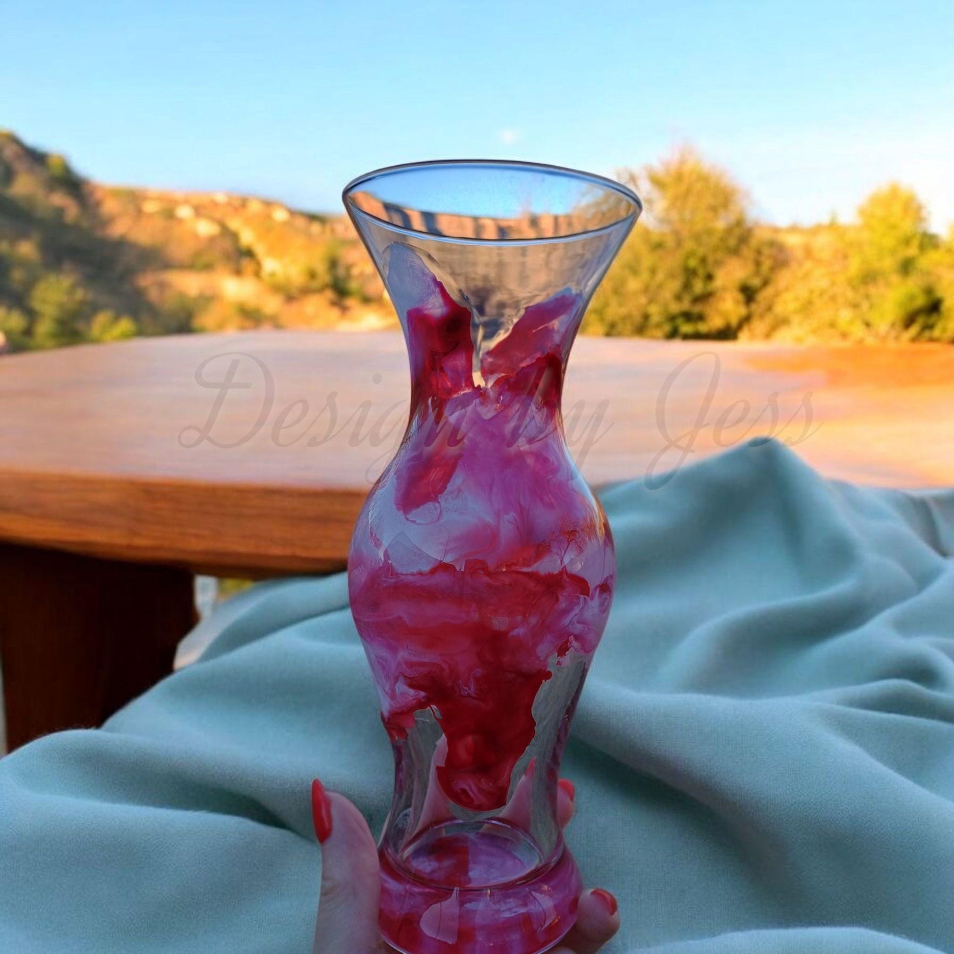 Glass vase with red and white abstract art resin and ink design held by a hand on a blue blanket outdoors. A Style by Jess at Gotta Have It Design