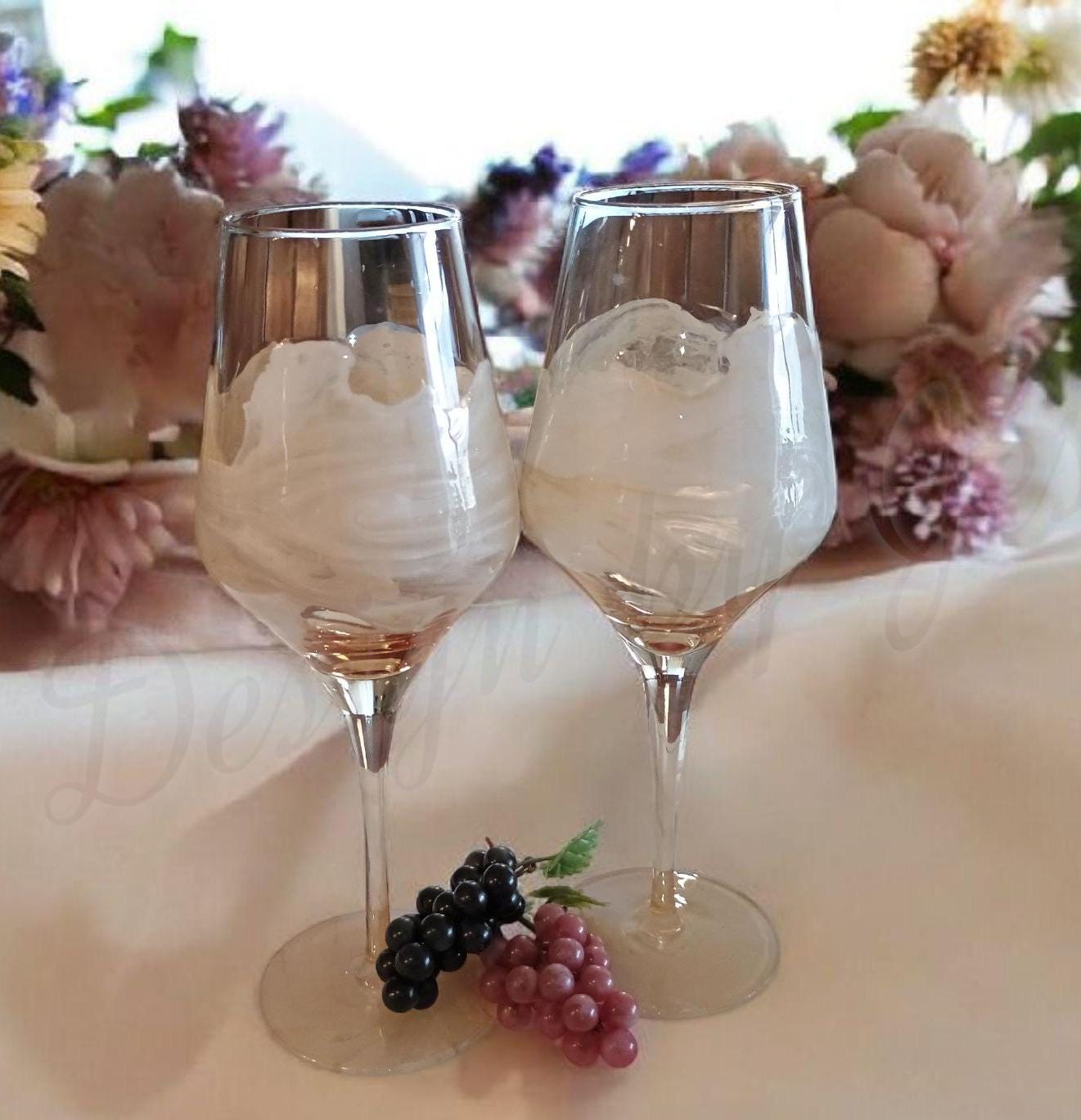 Two wine glasses with  on a table with flowers and grapes.