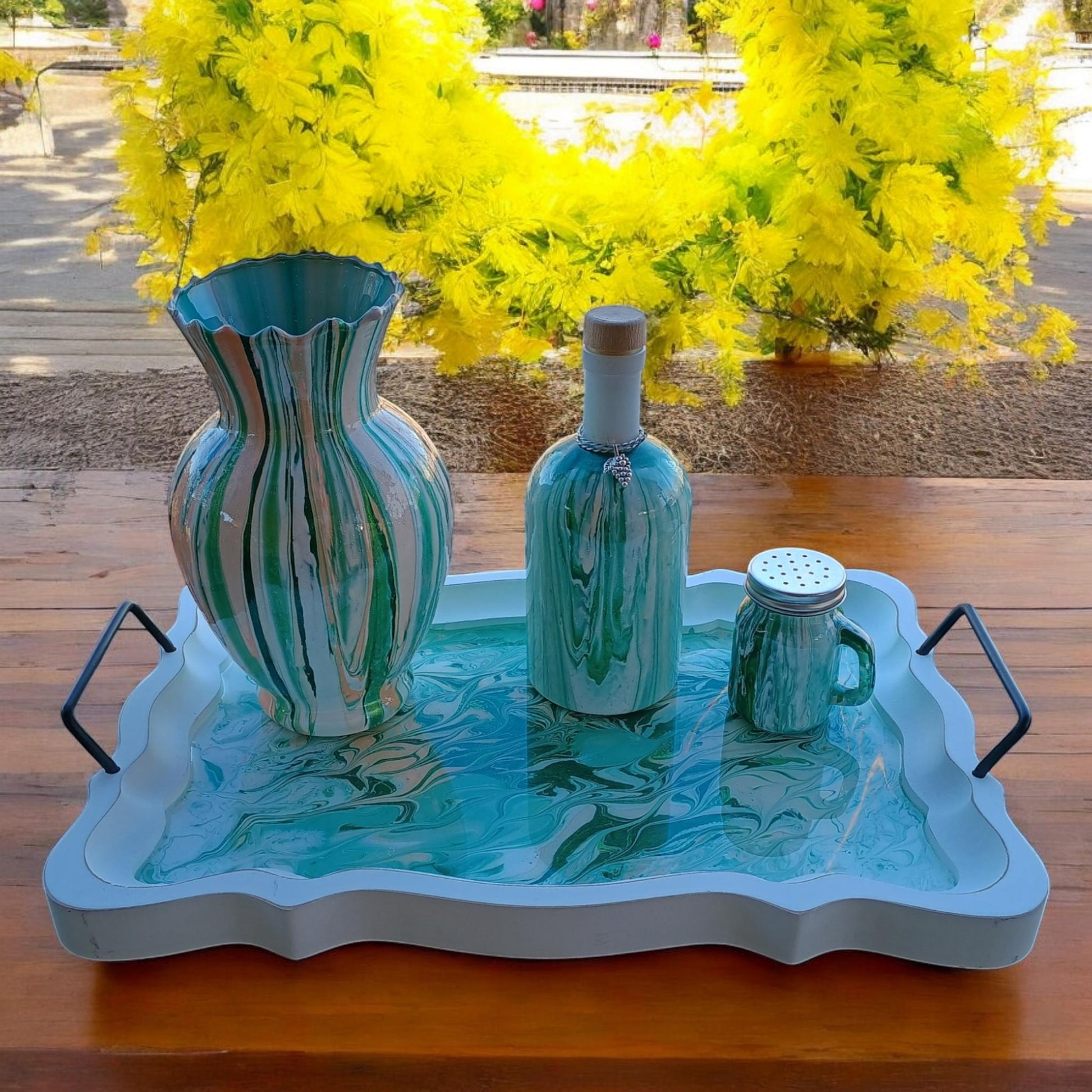 Decorative items including a vase, bottle, and mug on a tray with yellow flowers in the background.