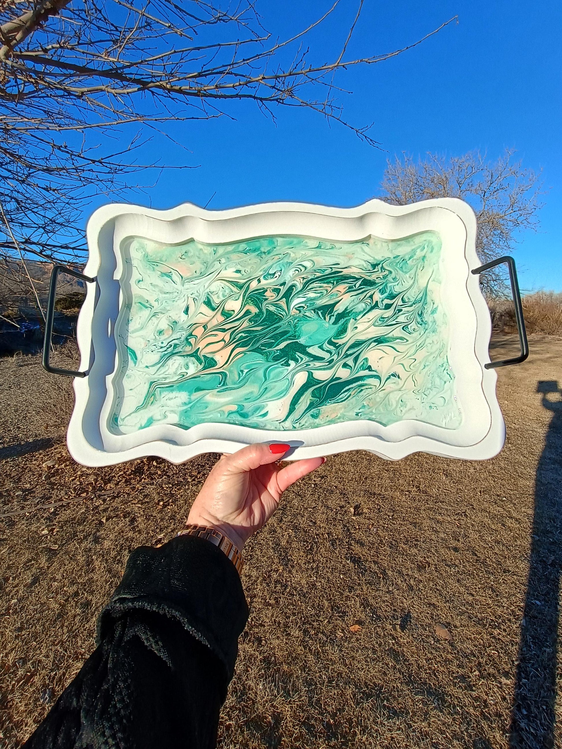 Person holding a decorative tray with a marbled design outdoors on a clear day.