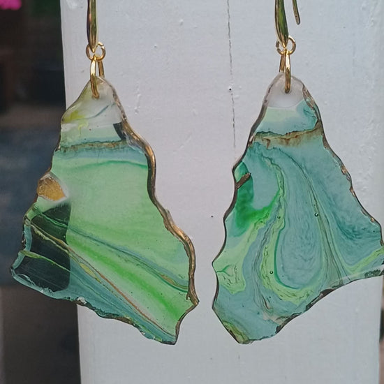 Video of abstract art statement earrings created with resin displaying a geode style with snow capped mountain white tops.  Video is filmed with a white background and pans to a nature setting.  A Style By Jess at Gotta Have It Design. 