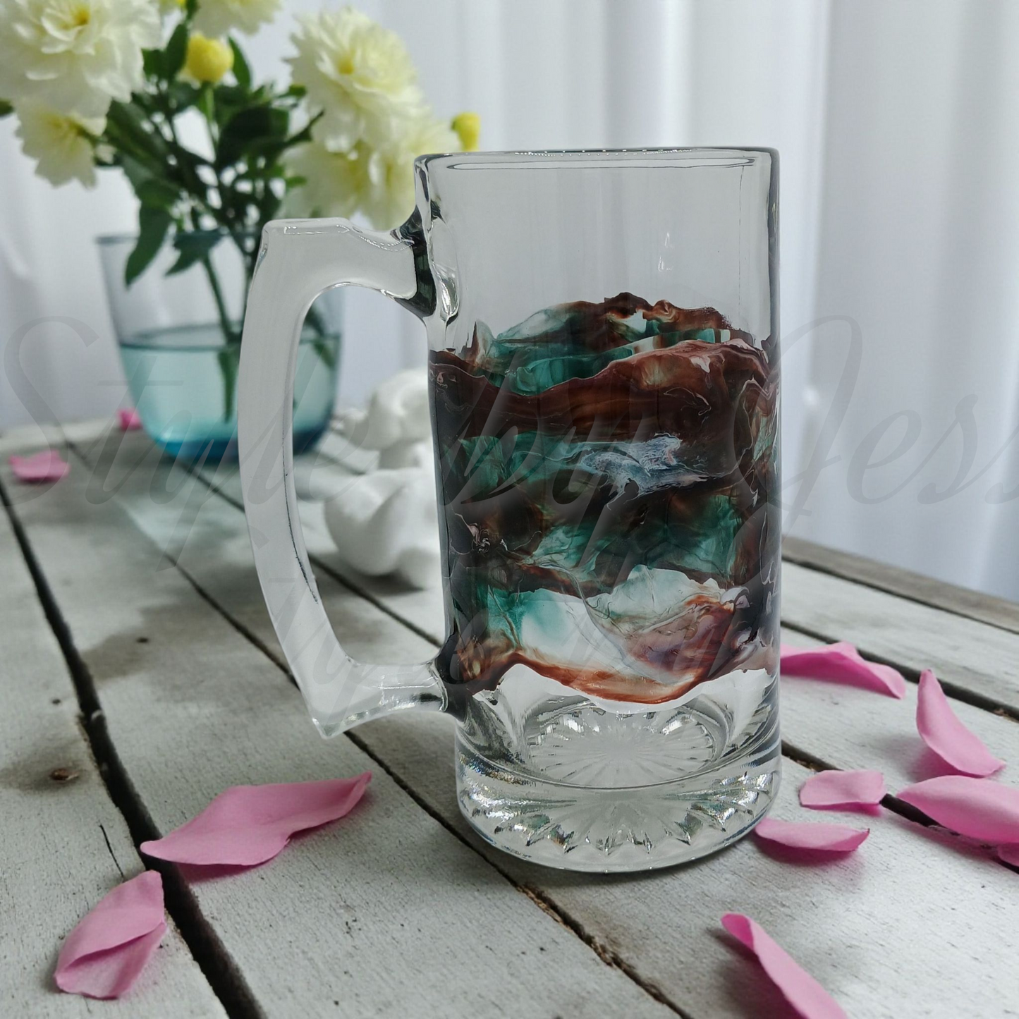 Oversized beer mug with an abstract design on the glass in a wedding setting with white roses and pink flower petals sitting on a rustic wood table featured as a wedding gift. 