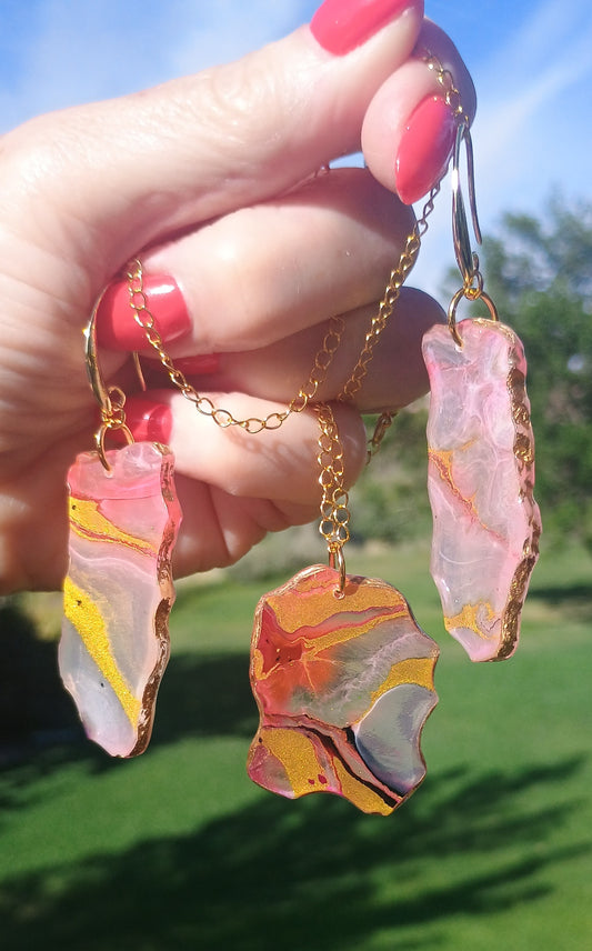 Handmade pink and gold marbled resin dangle earrings and pendant necklace set held outdoors — one-of-a-kind wearable art jewelry by Style By Jess
