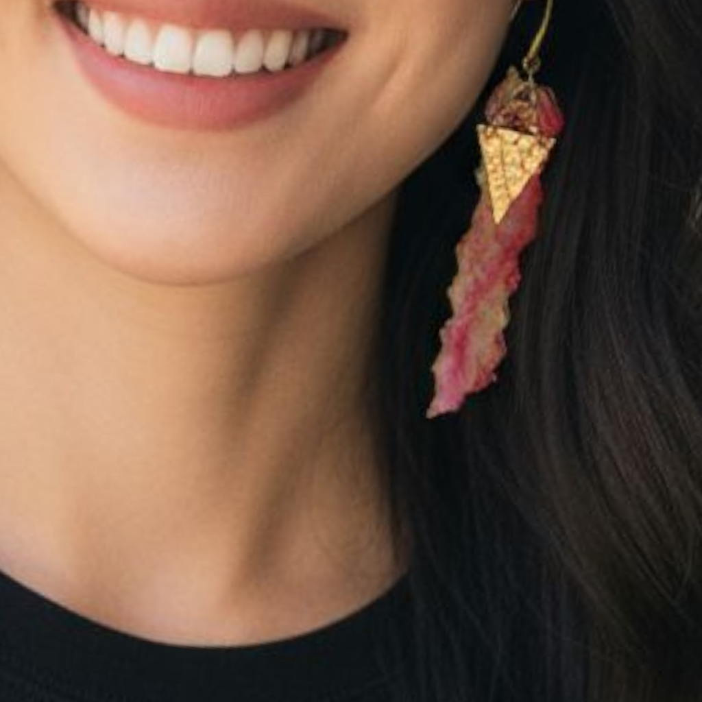Close-up of a person wearing a unique earring with a gold triangle and pink feather-like design.