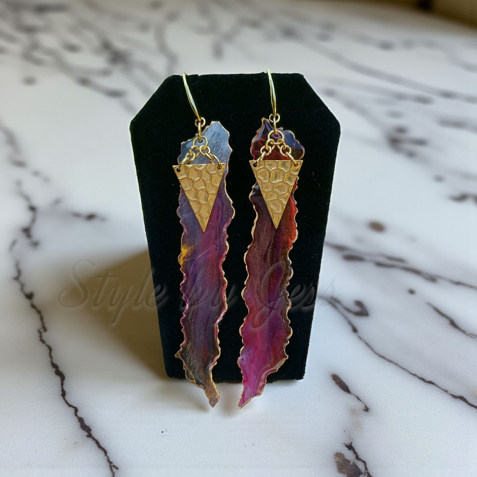 Pair of earrings on a black stand with a marble background