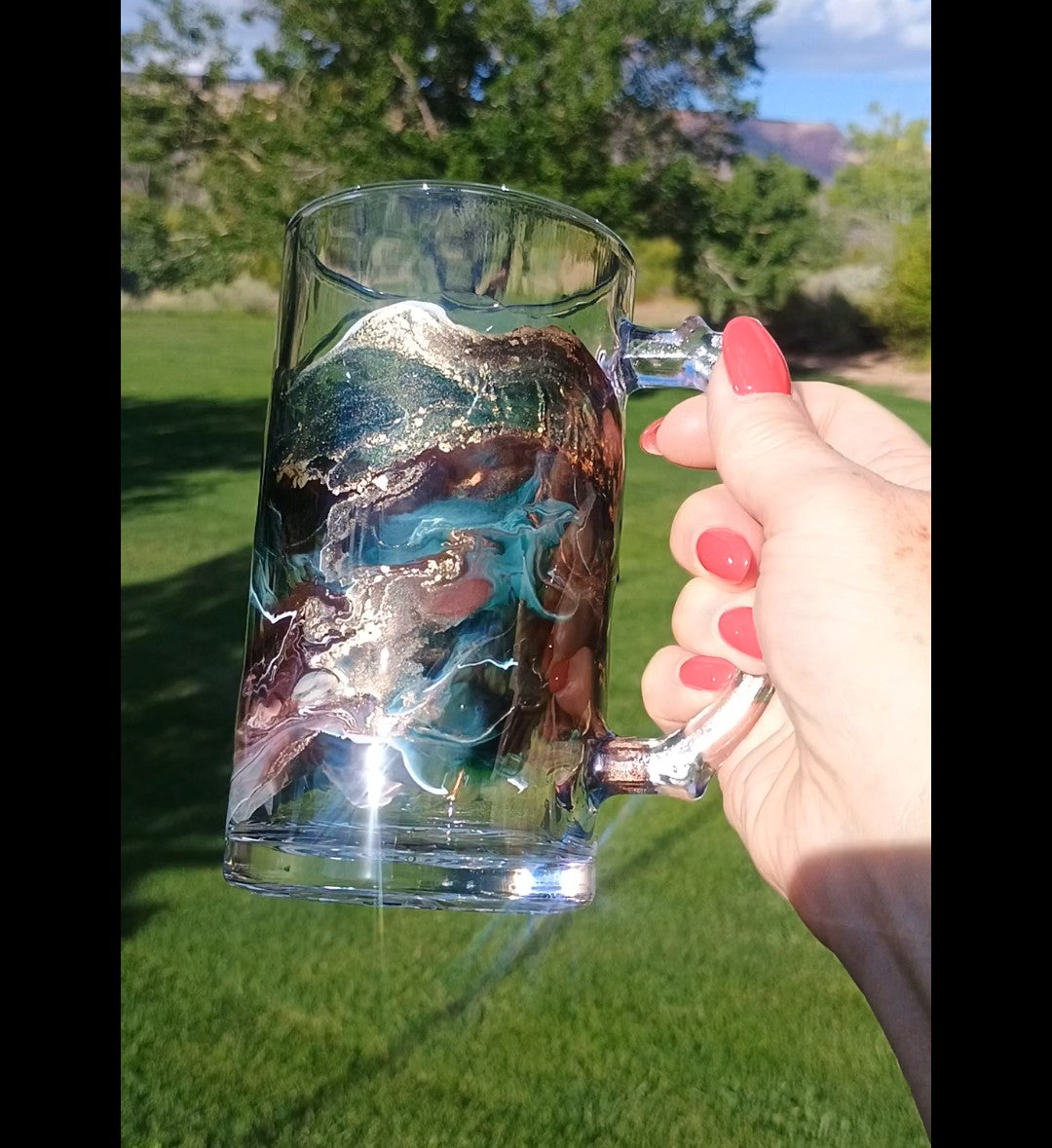 Handmade resin art beer mug with teal, brown, white and gold abstract design, held outdoors a Style by Jess at Gotta Have It Design