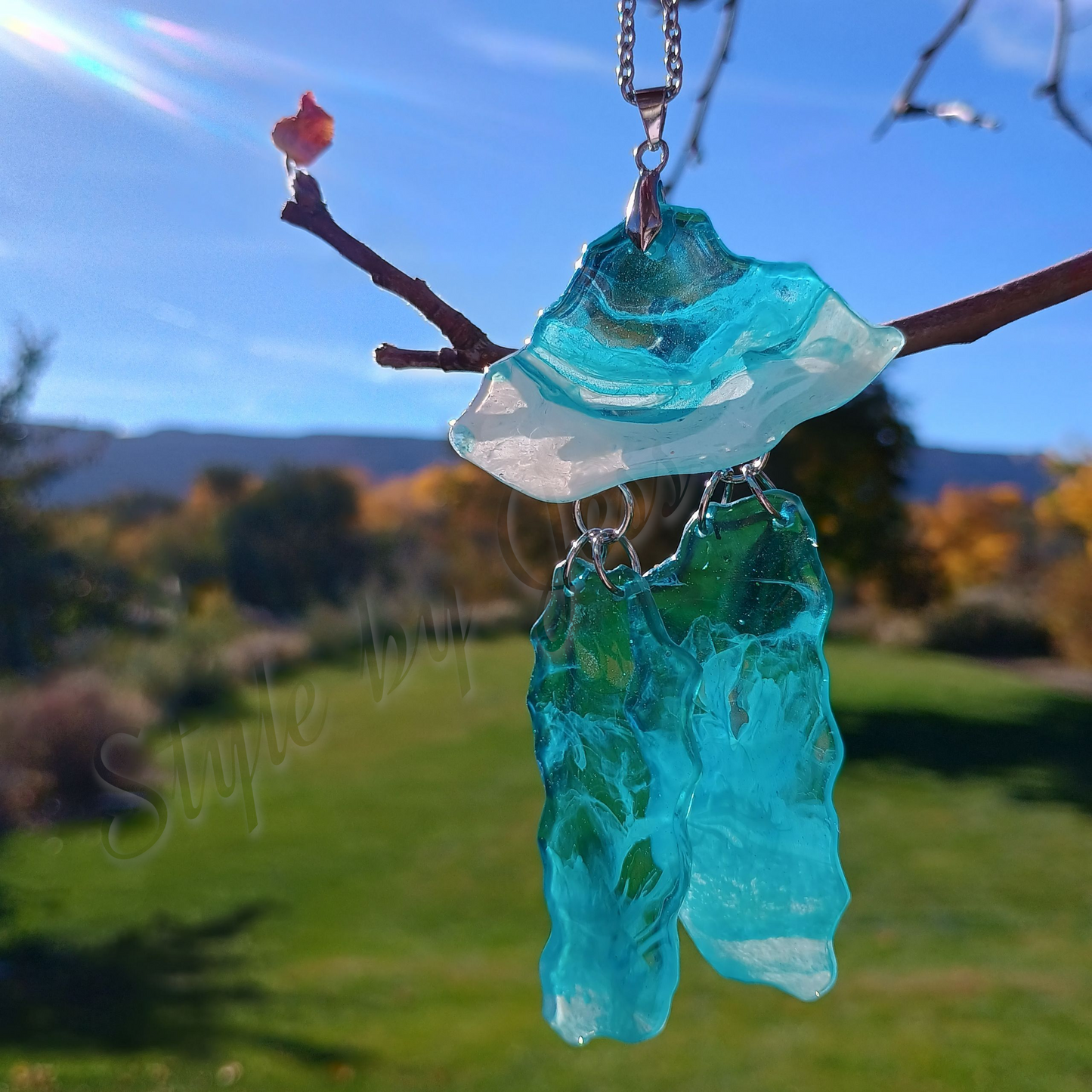Blue and white sea glass style pendant on a branch with a blurred outdoor background
