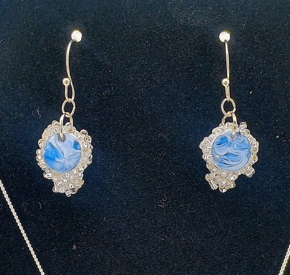 A pair of silver-toned drop earrings with oval blue marbled centers and textured silver borders, displayed on a black velvet jewelry stand.