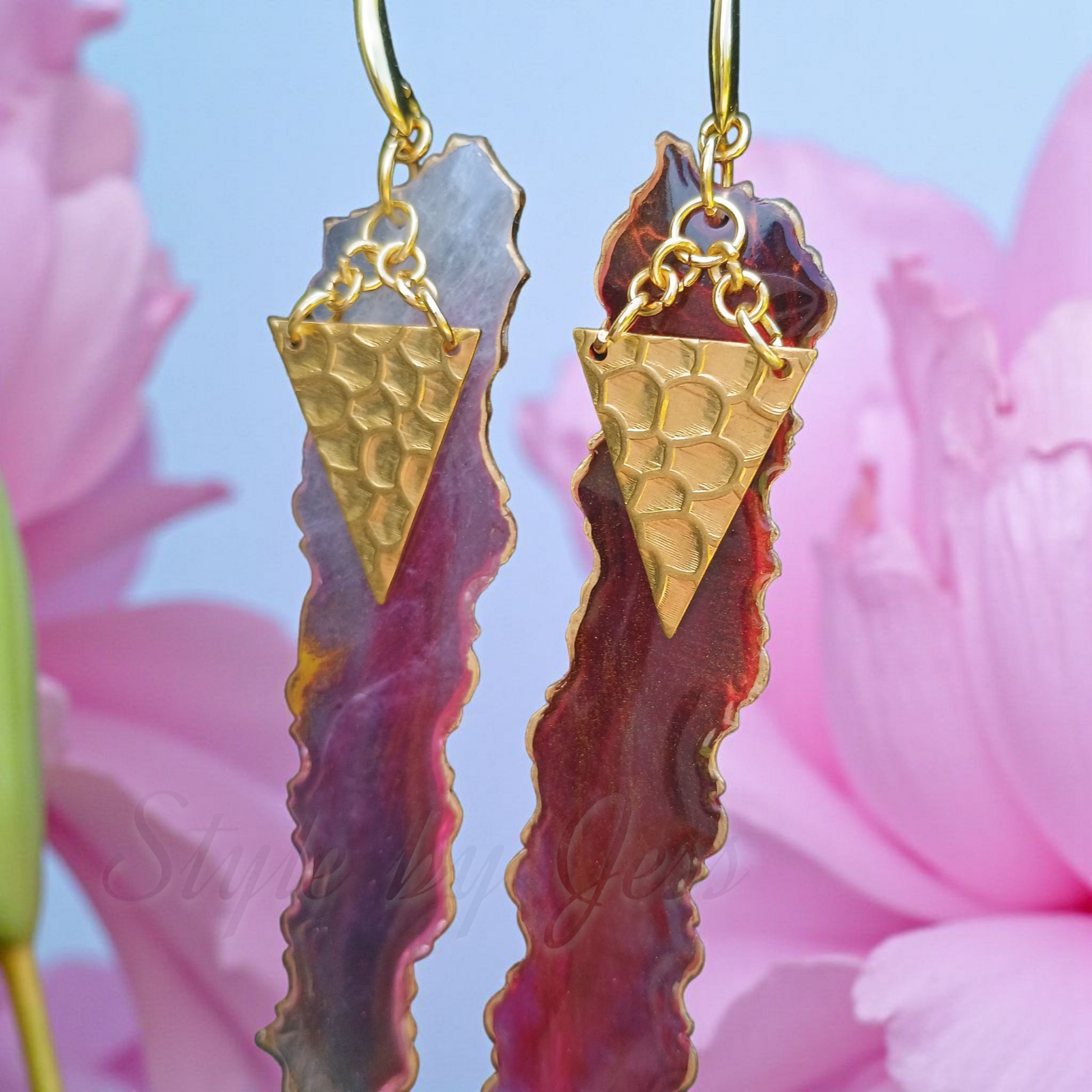 Gold and red earrings with textured design against a pink floral background