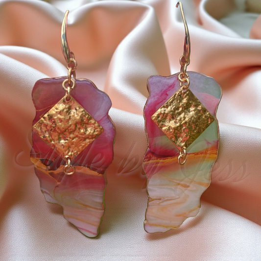 Pair of earrings with gold accents and colorful stones on a soft pink fabric background