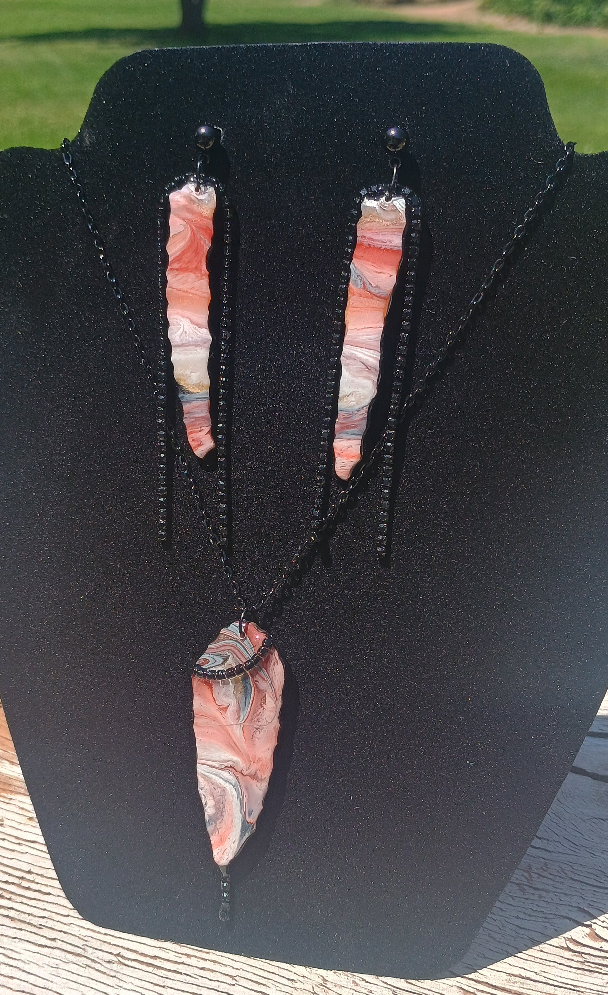 Handmade resin pendant necklace held in hand outdoors — earth tone marble swirls in terracotta, blush, and sage with black shimmery beaded edge trim and black chain, by Style By Jess at Gotta Have It Design
