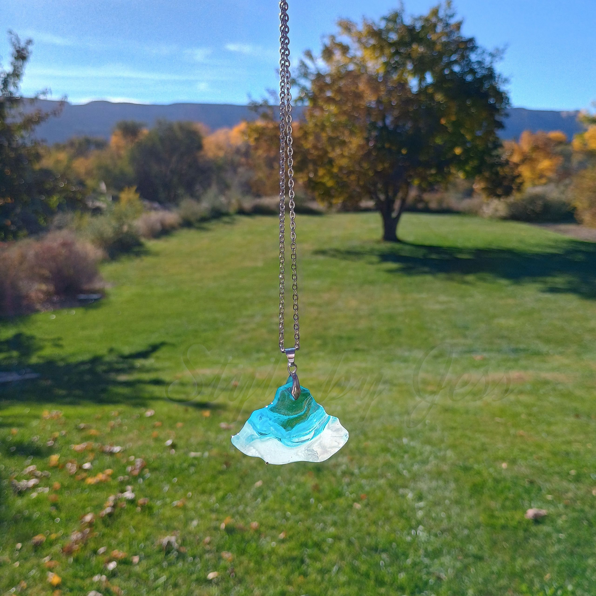 Necklace with a blue and white pendant in front of a grassy field with trees.