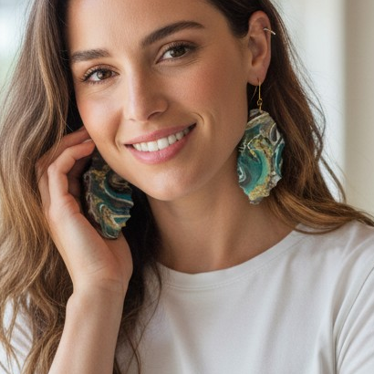 Woman in a casual setting, possibly a cafe, wearing a white t-shirt and blue jeans displaying colorful abstract art resin dangle earrings that are handmade a Style By Jess at Gotta Have It Design
